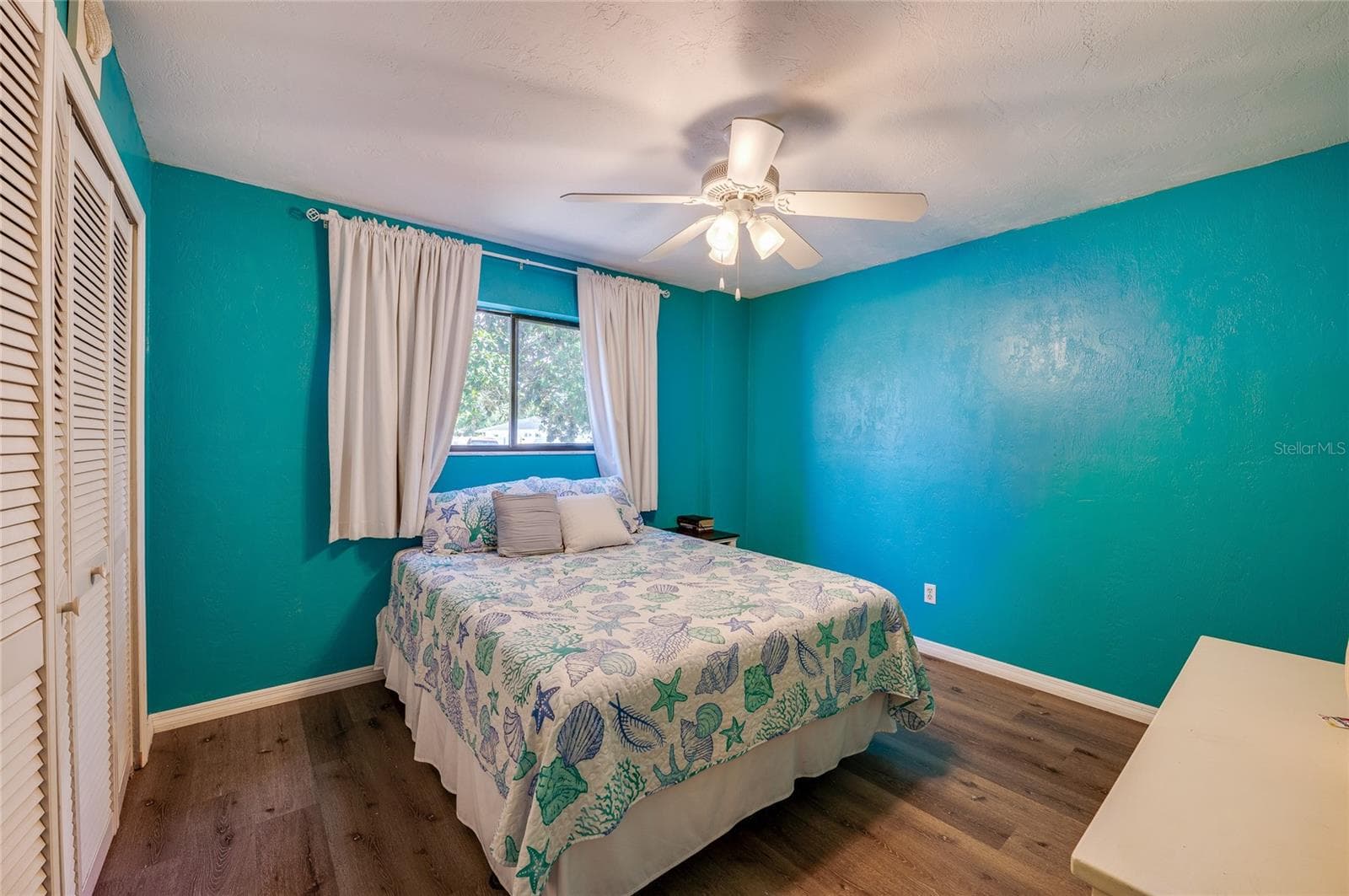 Vibrant coastal-themed bedroom accented with bright turquoise walls, modern LVP flooring, and a ceiling fan. Double closet doors offer ample storage space. - 146 WESTWOOD DR, DAYTONA BEACH