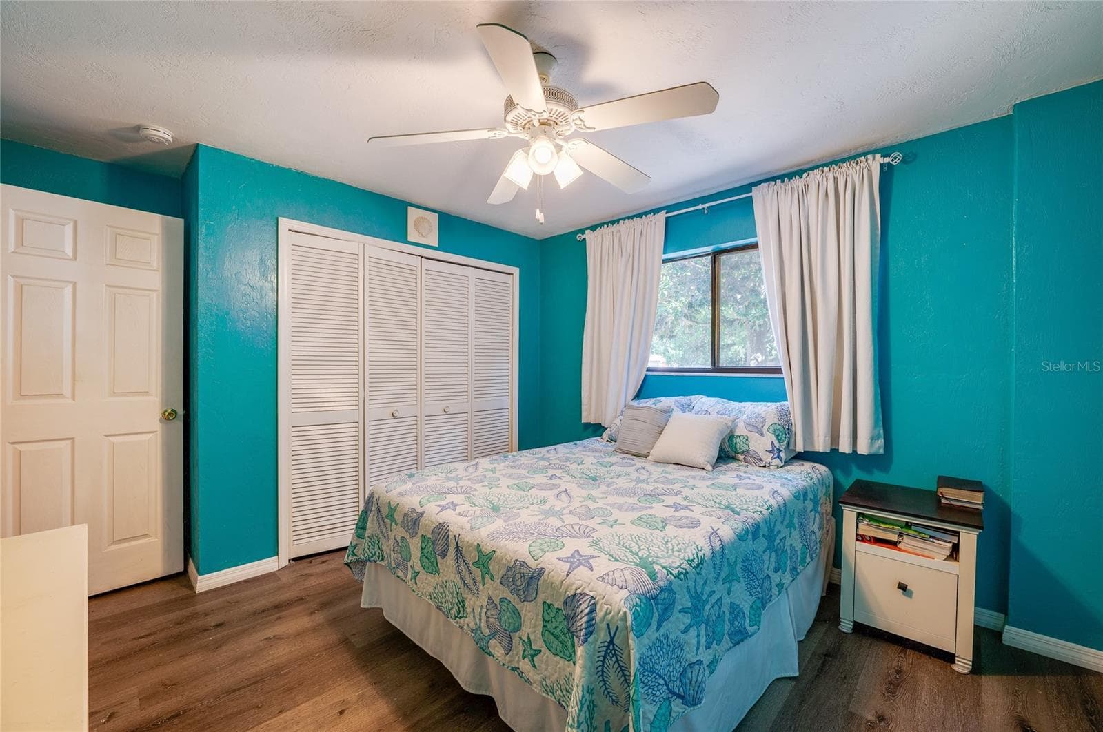 Bright bedroom showcasing vibrant blue walls, light-toned LVP flooring, and double louvered closet doors under a classic white ceiling fan. - 146 WESTWOOD DR, DAYTONA BEACH