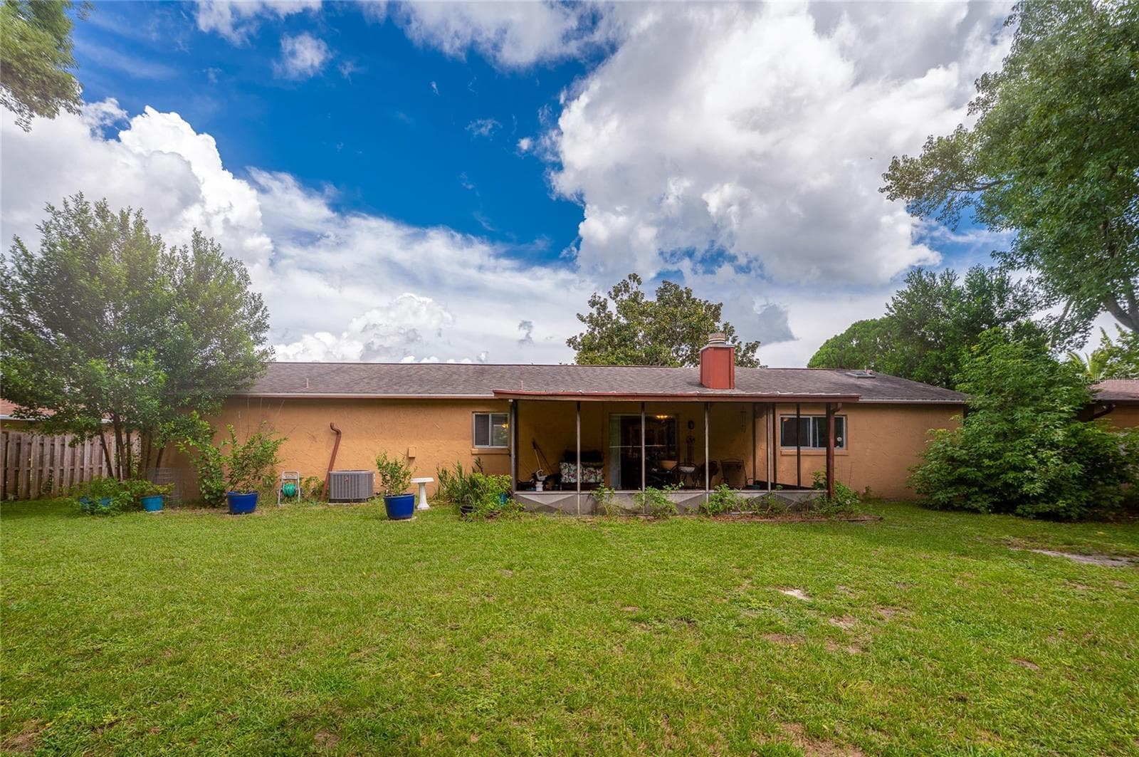 Rear view of the single-story home featuring a screened back patio, exterior HVAC unit, potted plants, and a spacious green lawn. - 146 WESTWOOD DR, DAYTONA BEACH