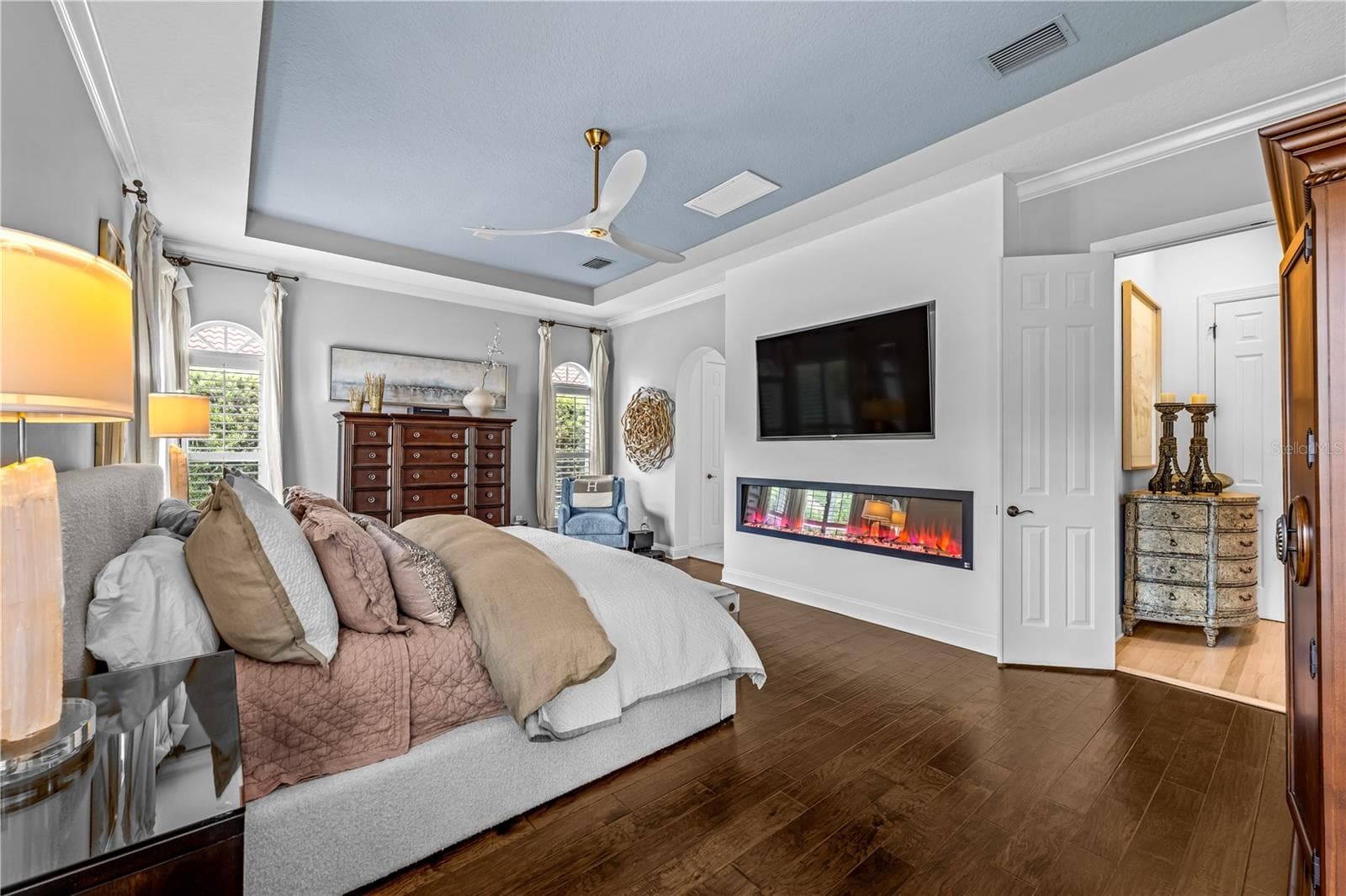 Tray ceiling, dark wood flooring, linear electric fireplace with mounted TV, and arched doorway. - 1921 FLORESTA VIEW DR, TAMPA