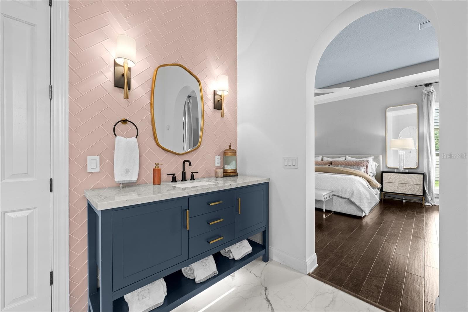 Navy vanity with stone top, pink herringbone tile wall, brass mirror, and arched view to the bedroom. - 1921 FLORESTA VIEW DR, TAMPA