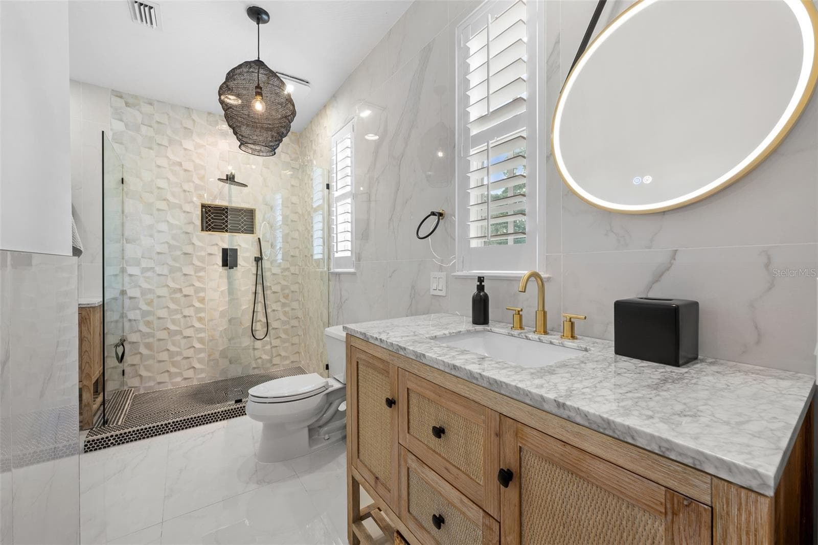Second Bathroom (upstairs) - Walk-in shower with black fixtures, wood vanity with stone top, and brass-framed round mirror. - 1921 FLORESTA VIEW DR, TAMPA