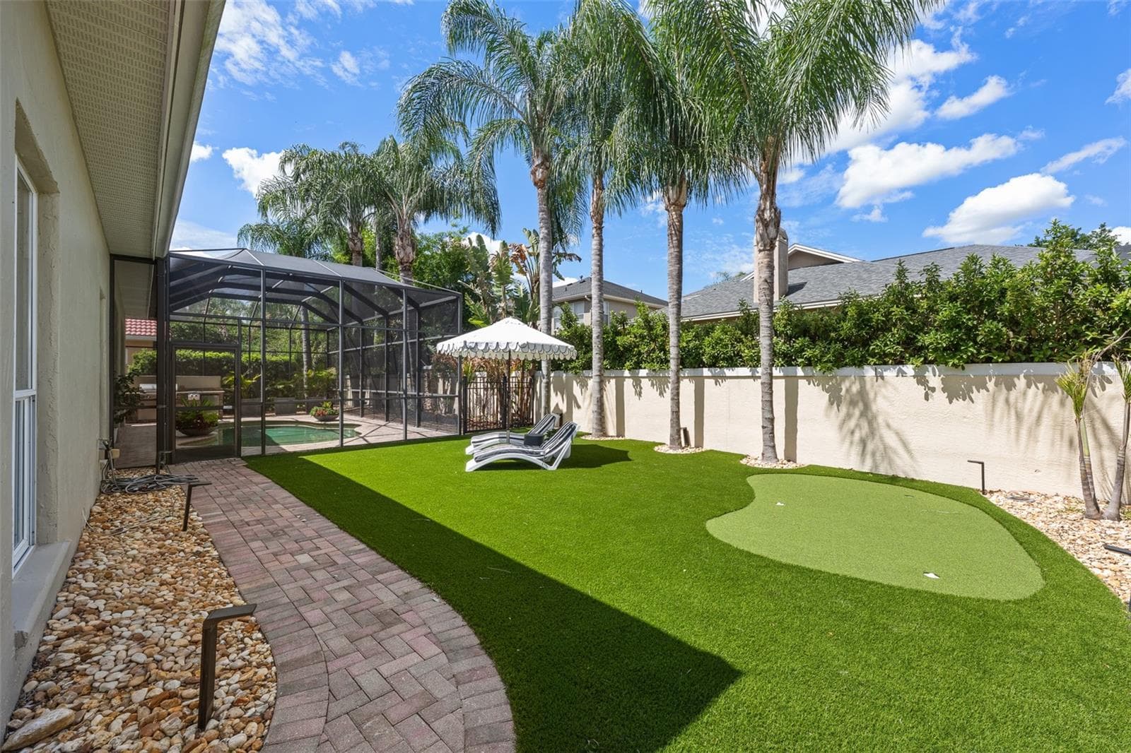 Artificial turf putting green with paver path and screen-enclosed pool beyond. - 1921 FLORESTA VIEW DR, TAMPA