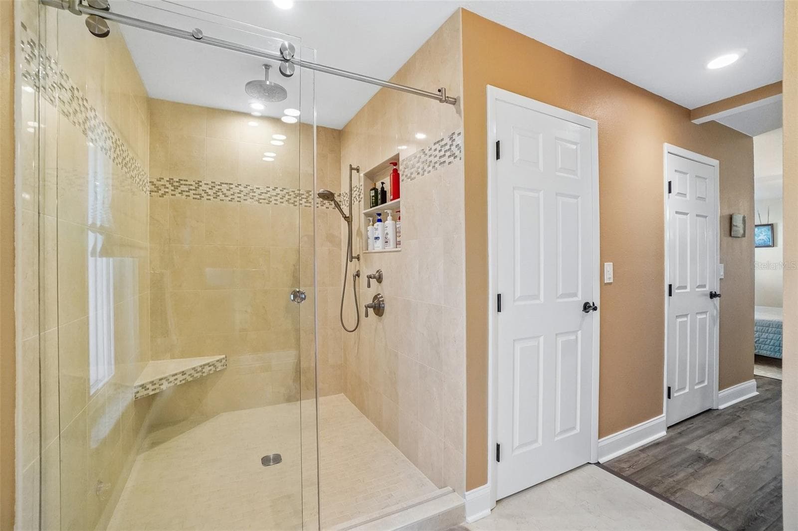 Primary Ensuite Bathroom – The primary bath features a large walk-in shower with frameless glass, full-height tile, a decorative mosaic accent band, built-in bench, rainfall showerhead, and handheld shower fixture. - 971 CORTLAND WAY, PALM HARBOR