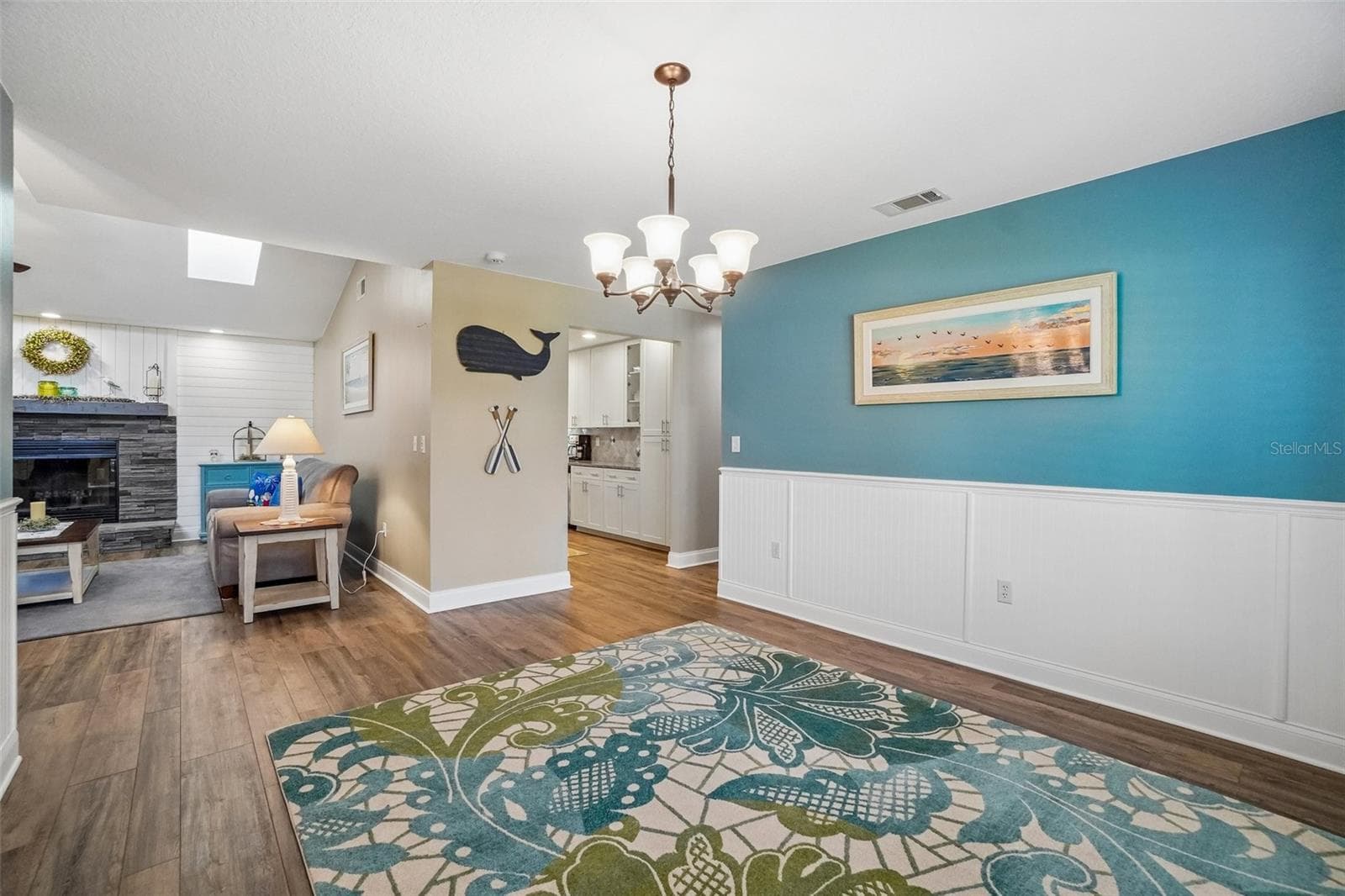 Dining Room – This open dining area features wood-look flooring, white beadboard wainscoting, and a chandelier, with an easy visual connection to the living room and kitchen for a cohesive main living layout. - 971 CORTLAND WAY, PALM HARBOR