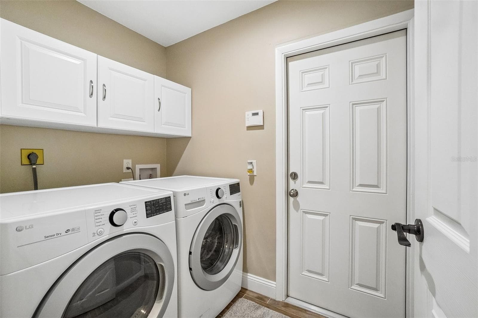Laundry Room – The dedicated laundry room offers side-by-side laundry appliances, overhead cabinetry for added storage, and a convenient exterior access door. - 971 CORTLAND WAY, PALM HARBOR