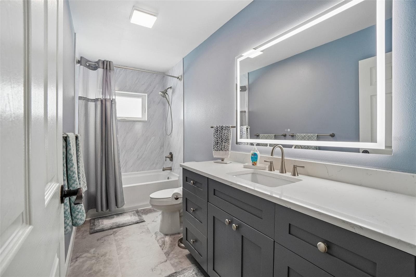 Second Bathroom – The second full bath features a dark shaker-style vanity with a light countertop, an illuminated mirror, and a tub/shower combination with a clean, contemporary surround. - 971 CORTLAND WAY, PALM HARBOR
