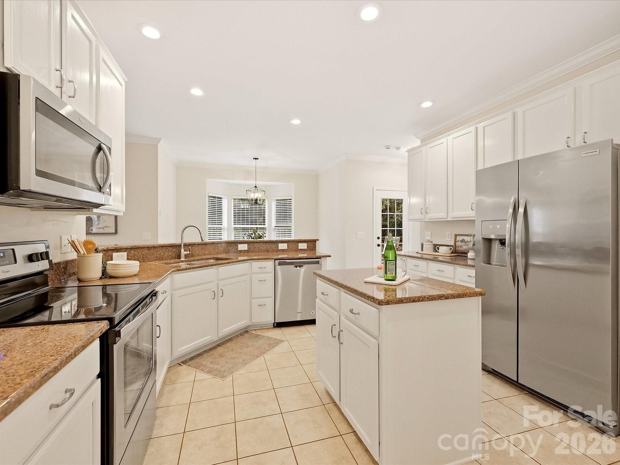 The bright kitchen features crisp white cabinetry, granite countertops, stainless steel appliances, a center island, and an open layout that connects easily to the surrounding living spaces. - 16006 Lavenham Road, Huntersville