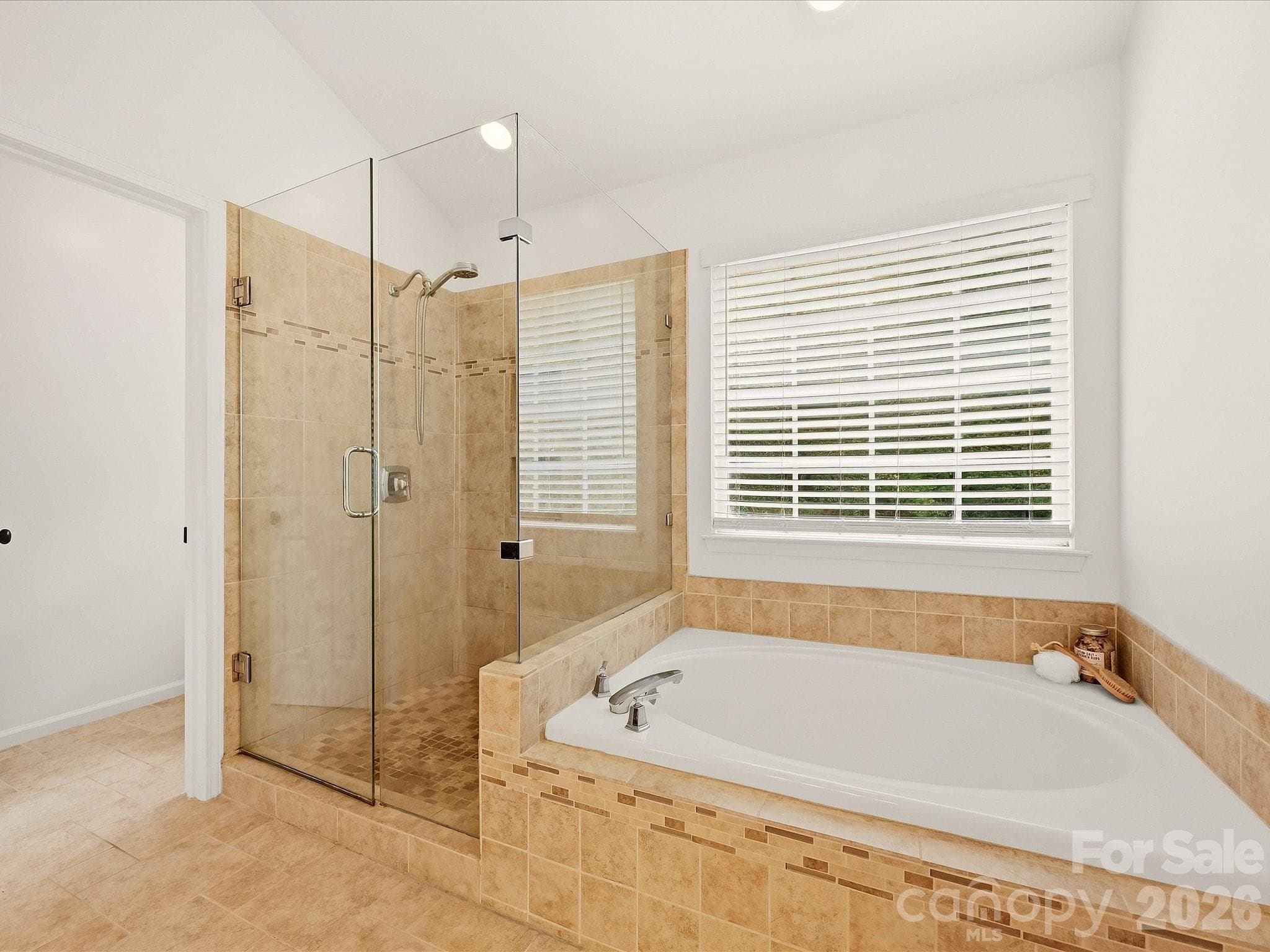 The primary bath features dual vanities, a garden tub, a separate glass-enclosed shower, and abundant natural light for a bright, relaxing retreat. - 16006 Lavenham Road, Huntersville