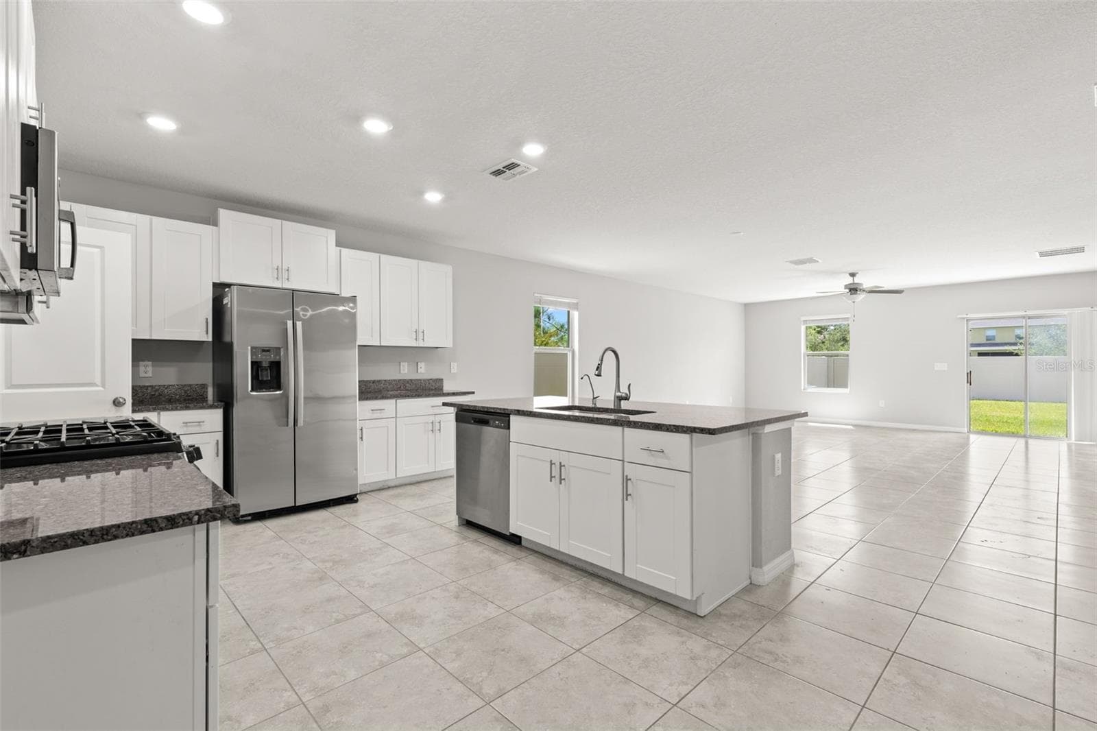 The kitchen opens directly to the main living area, with white cabinetry, granite countertops, stainless appliances and a large island with sink and dishwasher. Recessed lighting and tile flooring carry the clean, neutral finish through the heart of the home. - 5061 WHITE CHICORY DR, APOLLO BEACH