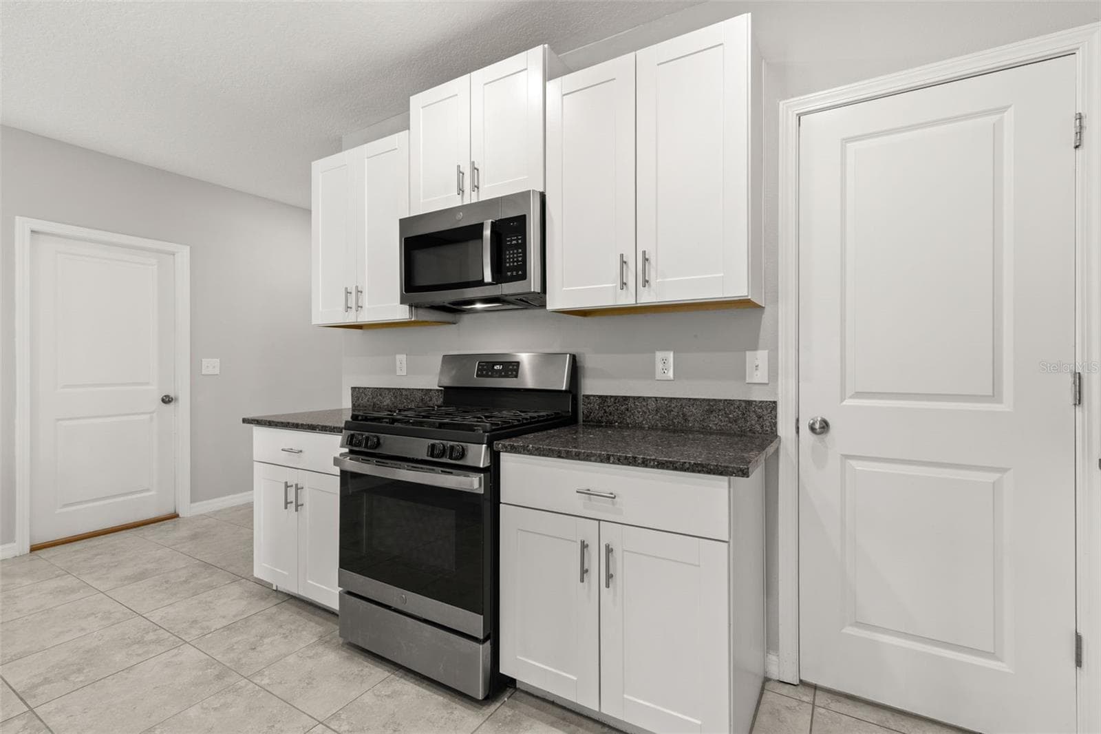 The kitchen pairs a gas range and built-in microwave with white shaker-style cabinetry and granite countertops, while tall upper cabinets add extra storage around the cooking area. - 5061 WHITE CHICORY DR, APOLLO BEACH