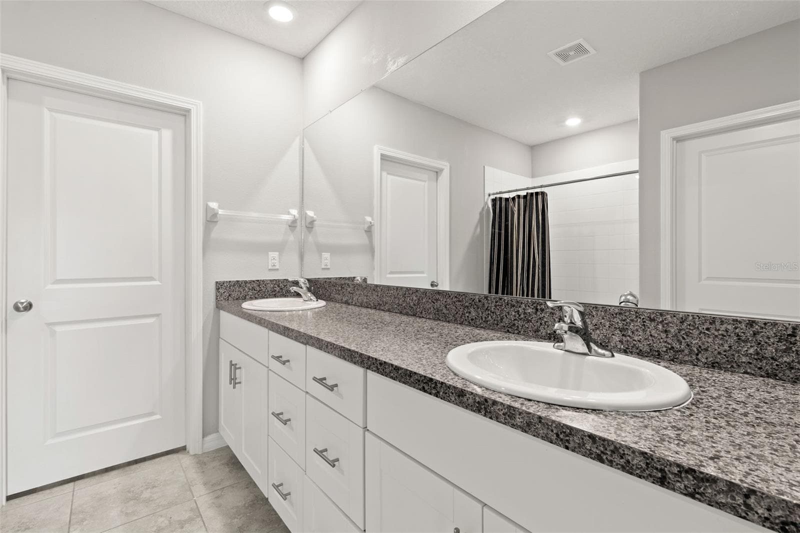 The primary ensuite bath features a long dual-sink vanity with granite countertops, generous storage, a large wall mirror and a tiled shower. - 5061 WHITE CHICORY DR, APOLLO BEACH