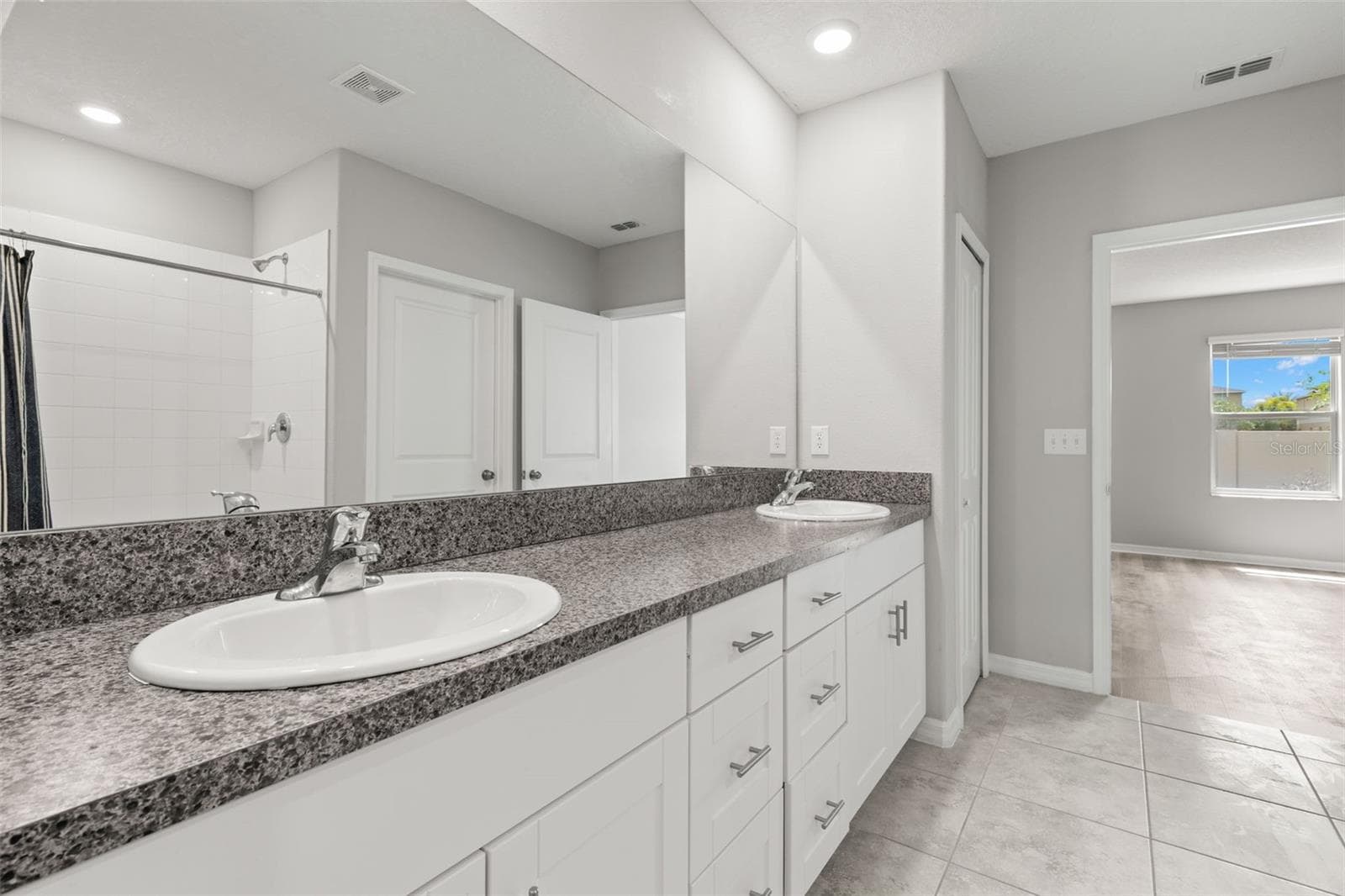 The primary bath’s long dual-sink vanity pairs granite countertops with generous storage, while the oversized mirror and recessed lighting keep the space bright and practical. - 5061 WHITE CHICORY DR, APOLLO BEACH