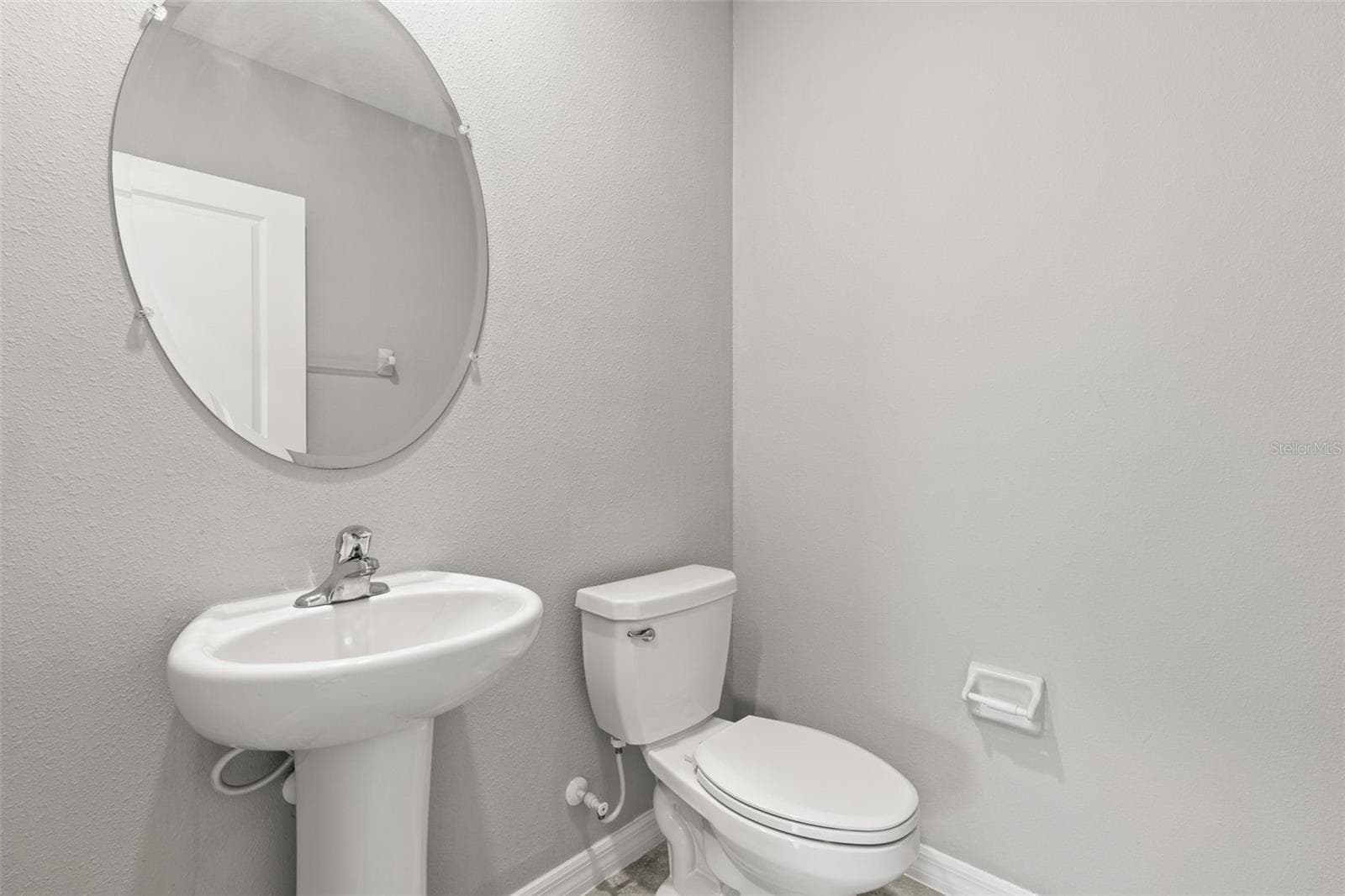 The main-level half bath features a pedestal sink, round mirror and fresh neutral finishes, providing convenient guest access just off the central living areas. - 5061 WHITE CHICORY DR, APOLLO BEACH