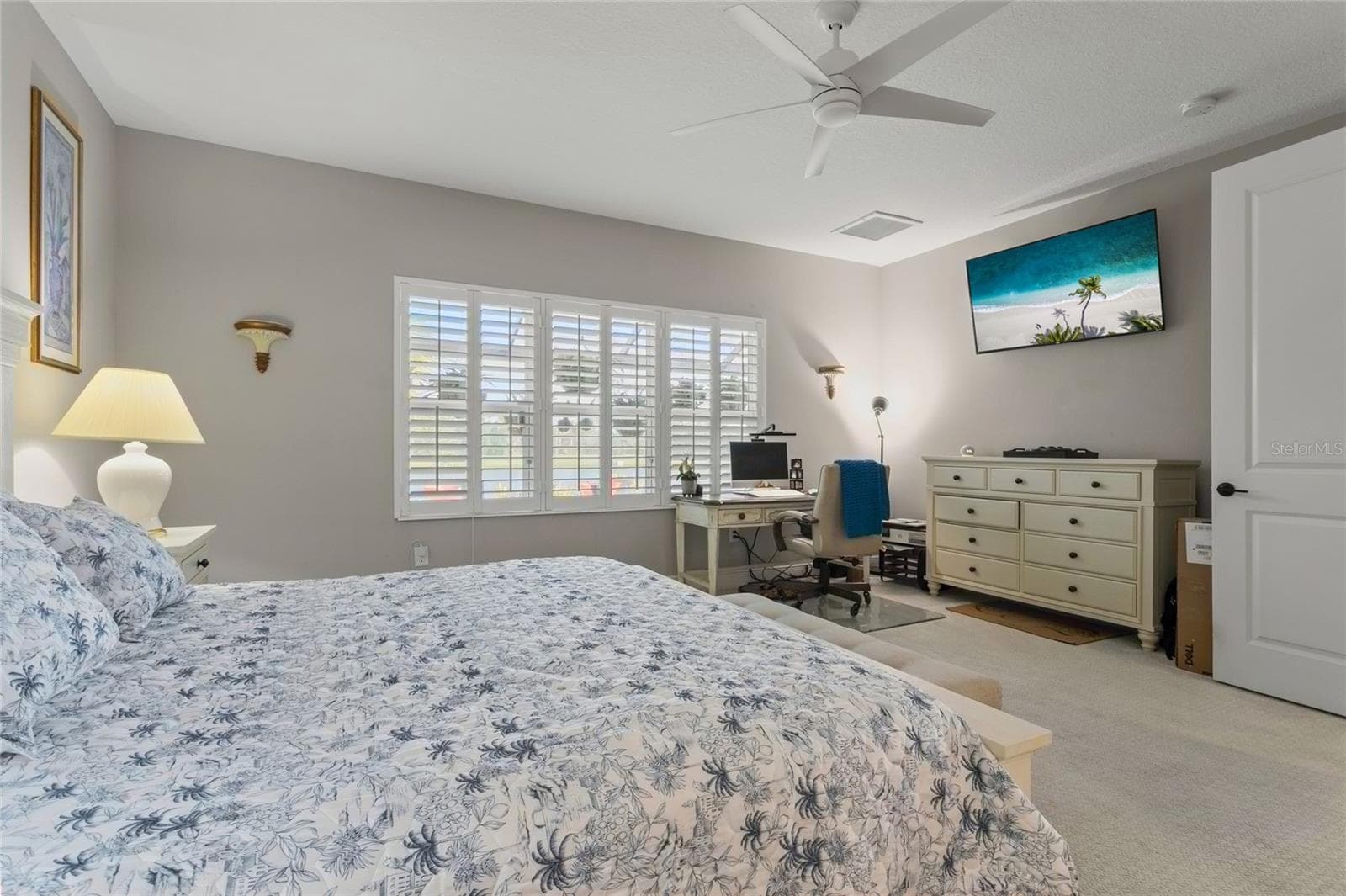 Bright primary bedroom with plantation shutters, neutral walls, ceiling fan, and a spacious layout that accommodates both rest and functionality. - 10625 FALLING LEAF CT, PARRISH
