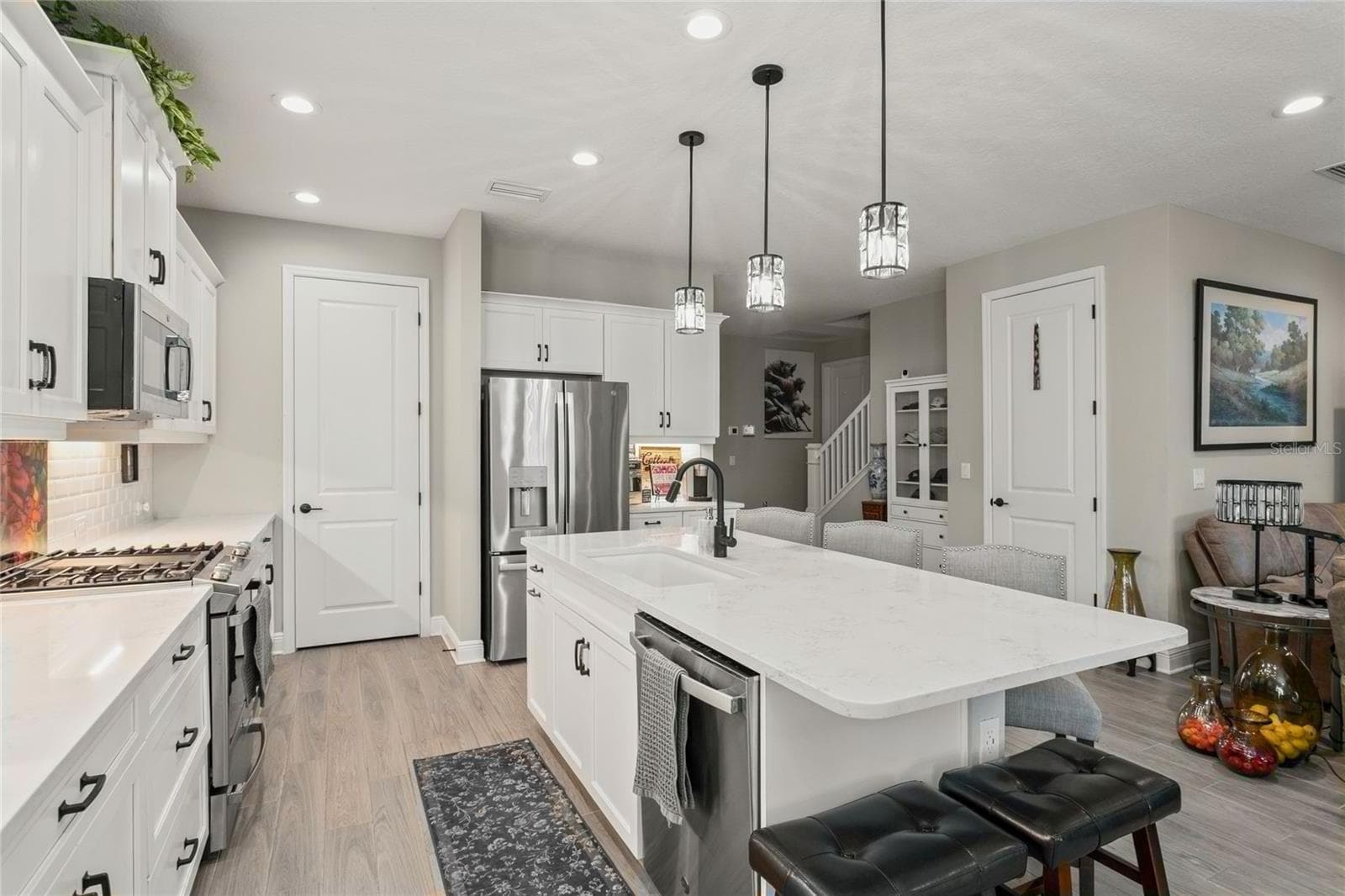 The kitchen further features a spacious center island with an integrated sink, pendant lighting, stainless-steel appliances, and white cabinetry with modern hardware, all flowing seamlessly into the open living area for an airy, connected feel. - 10625 FALLING LEAF CT, PARRISH