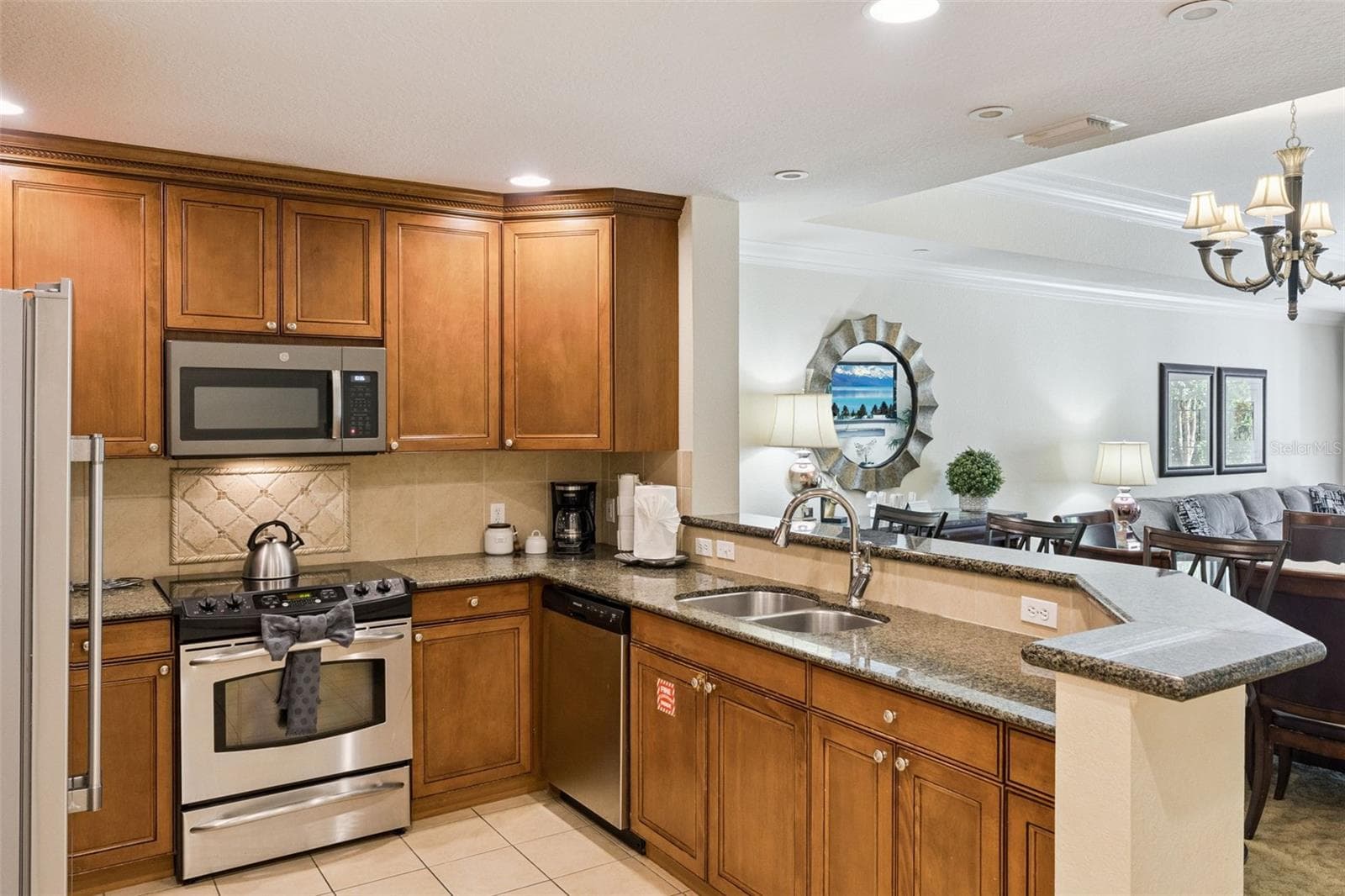 Fully Equipped Kitchen: Modern kitchen featuring warm wood cabinets, tile backsplash, granite counters, and full stainless steel appliances including a built-in microwave and range. - 7656 WHISPER WAY #102, REUNION