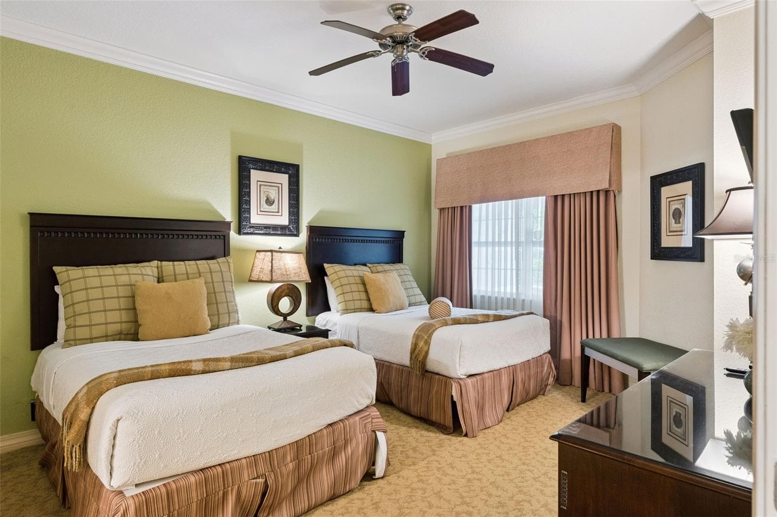 Double Guest Suite: Spacious guest bedroom offering two full beds, a soft green feature wall, central nightstand, ceiling fan, and a large draped window. - 7656 WHISPER WAY #102, REUNION