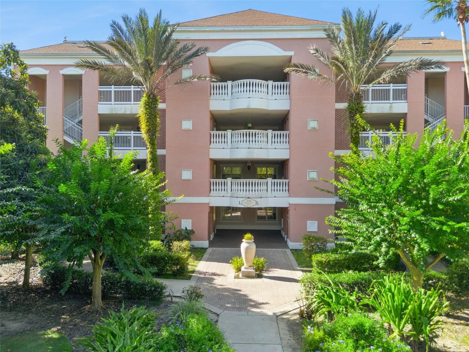 Building Exterior: Mediterranean-style exterior elevation featuring tropical palm trees, manicured landscaping, and a paver pathway leading to the main entrance. - 7656 WHISPER WAY #102, REUNION