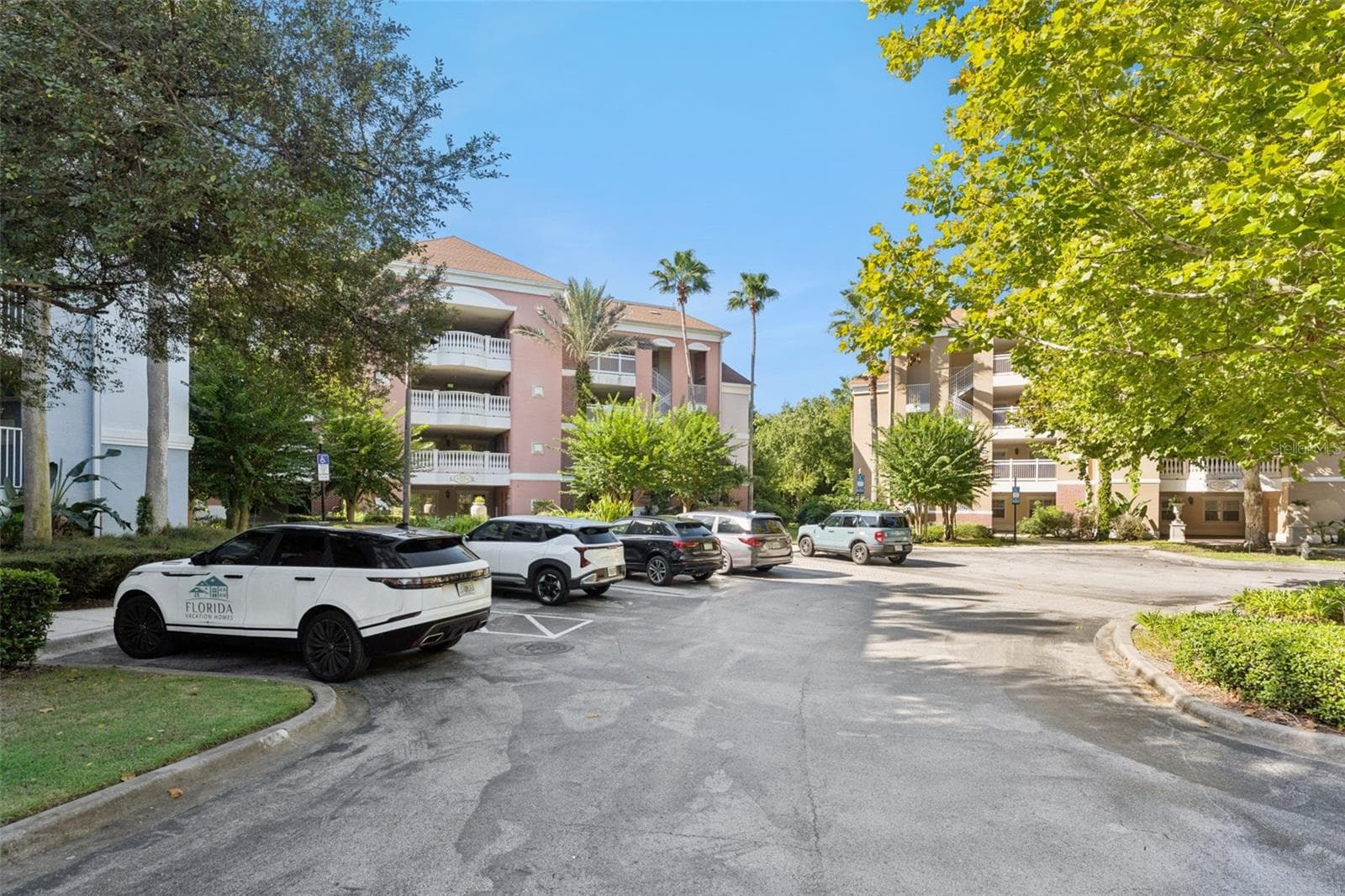 Community Parking: Ample surface parking area in front of the condo buildings, framed by mature trees and lush greenery. - 7656 WHISPER WAY #102, REUNION