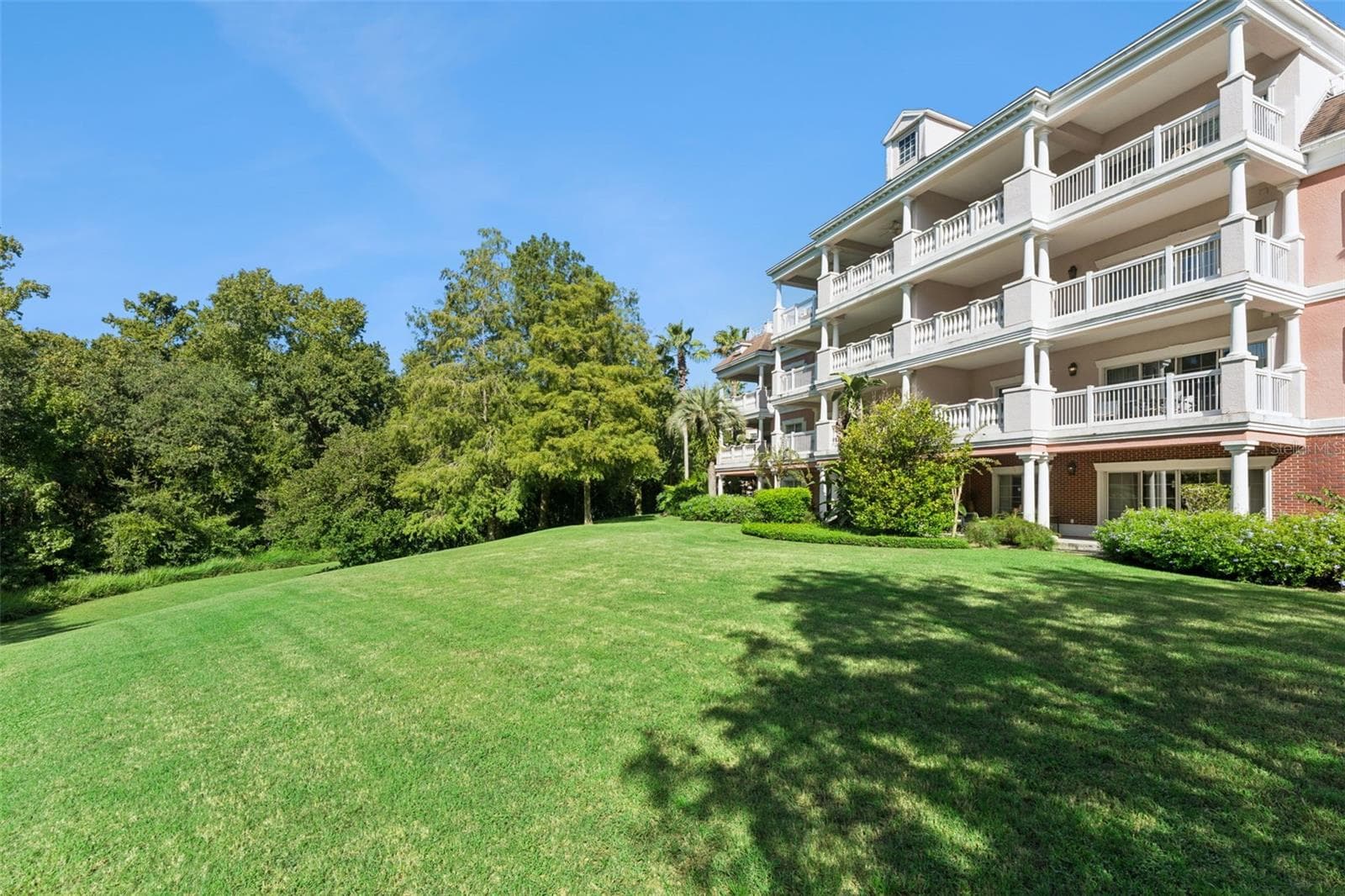 Building & Grounds View: Angled exterior view highlighting the sprawling lawn, shaded tree line, and private balconies of the condo community. - 7656 WHISPER WAY #102, REUNION