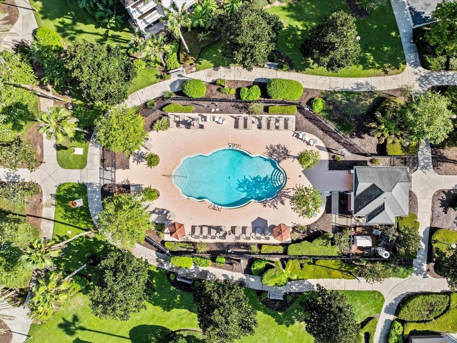Overhead View of Community Pool: Direct top-down aerial view of the sparkling community pool, paved sun deck with loungers, pool house, and manicured landscaping. - 7656 WHISPER WAY #102, REUNION