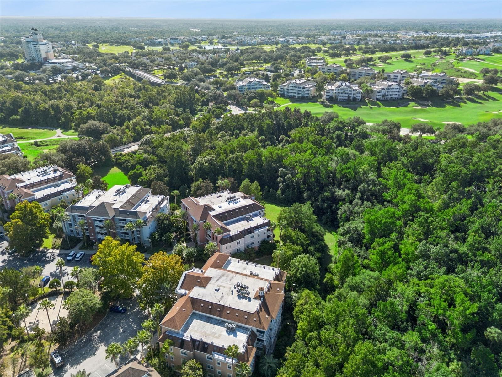 Aerial View of Complex: High-angle aerial capture showing the condo complex tucked into lush forest foliage adjacent to golf course fairways. - 7656 WHISPER WAY #102, REUNION