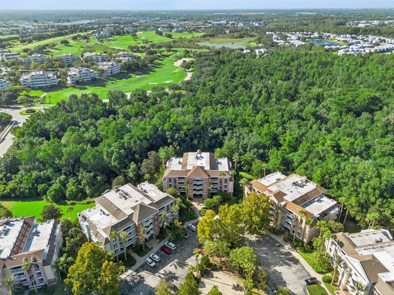 Aerial View of Building & Parking: High-angle aerial view of the condo building nestled directly against a lush conservation backdrop, featuring front parking access and nearby golf course views. - 7656 WHISPER WAY #102, REUNION