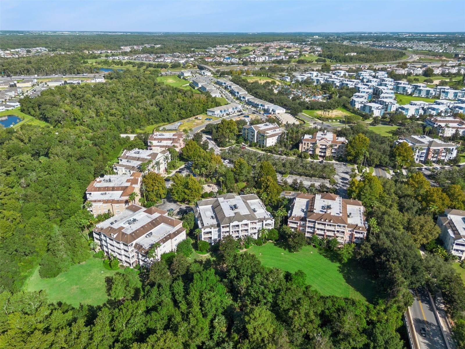 Community Layout Aerial: Broad aerial perspective showcasing the residential complex layout, expansive green spaces behind the buildings, and peaceful wooded surroundings. - 7656 WHISPER WAY #102, REUNION