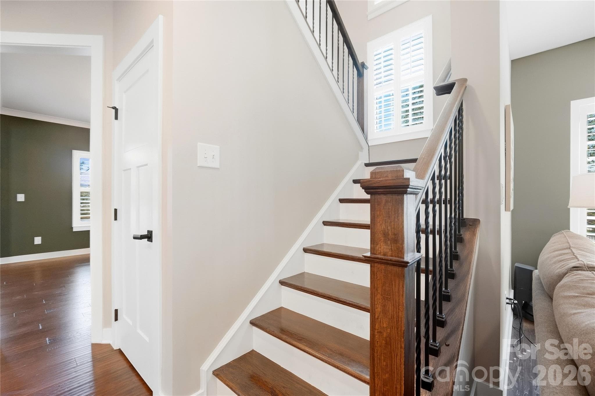 Staircase with wood treads, wrought-iron balusters, and a plantation-shuttered landing window. - 912 Manorwood Drive, Waxhaw
