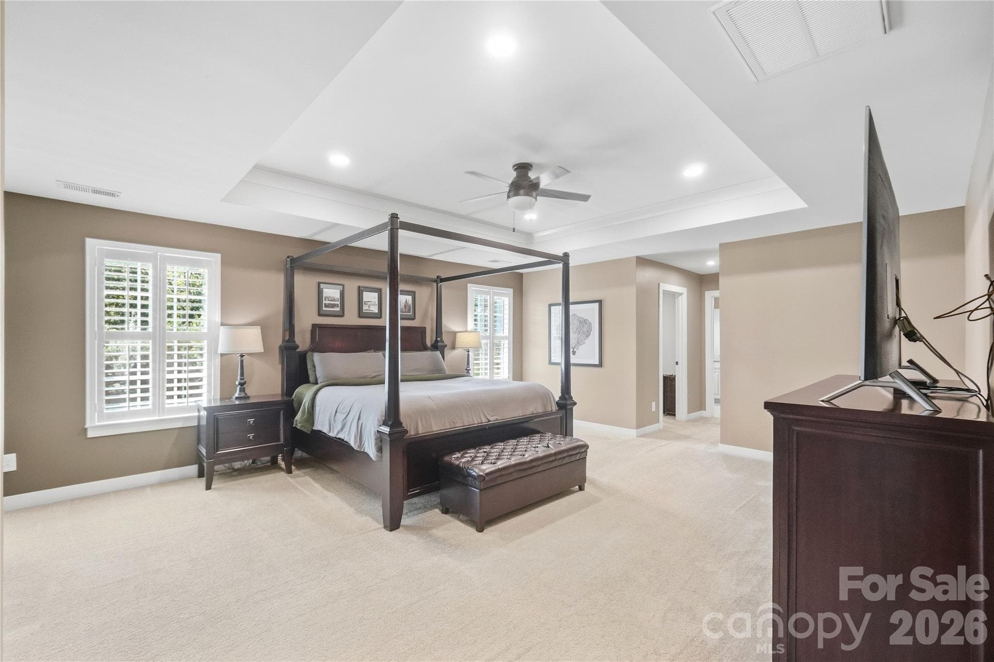 Spacious primary bedroom with a tray ceiling, ceiling fan, recessed lighting, and plantation shutters. - 912 Manorwood Drive, Waxhaw