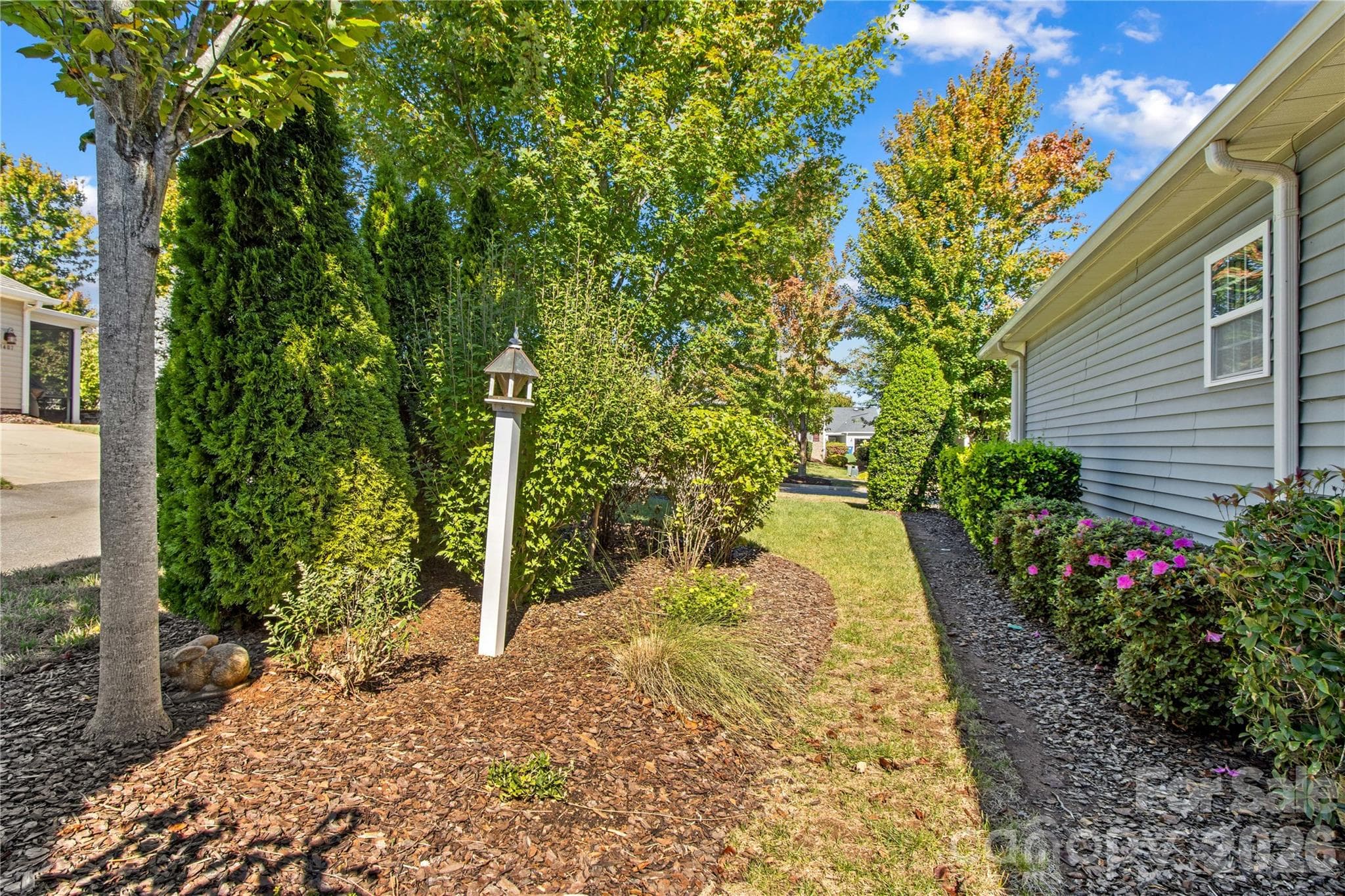Side yard has mature trees, blooming bushes, and grass areas. - 18114 Ebenezer Drive, Cornelius