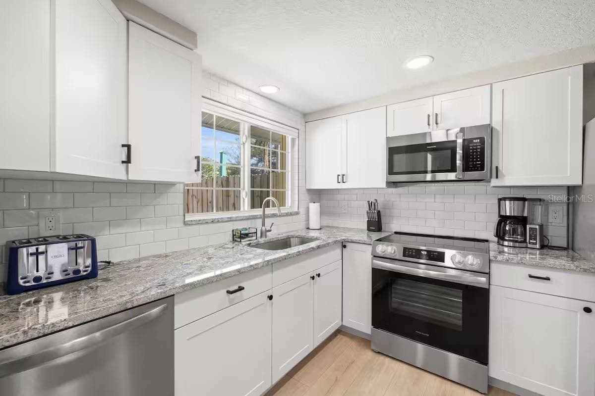 Crisp white cabinetry, stainless steel appliances, granite counters, and subway tile create a bright, fresh kitchen with plenty of workspace and storage. - 201 SOUTH ST, PALM HARBOR