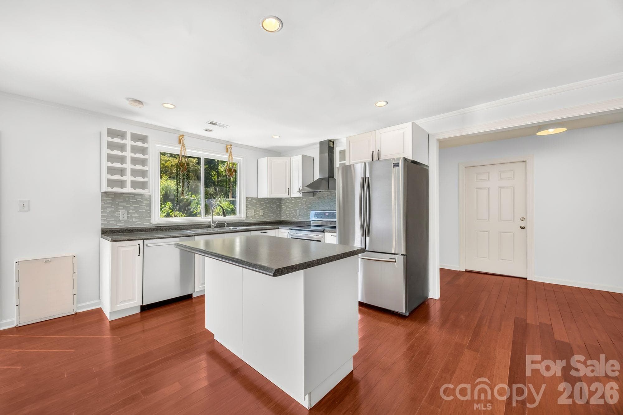 Updated kitchen with center island, white cabinets, tile backsplash and stainless steel appliances in a Charlotte ranch home - 4900 Cricklewood Lane, Charlotte