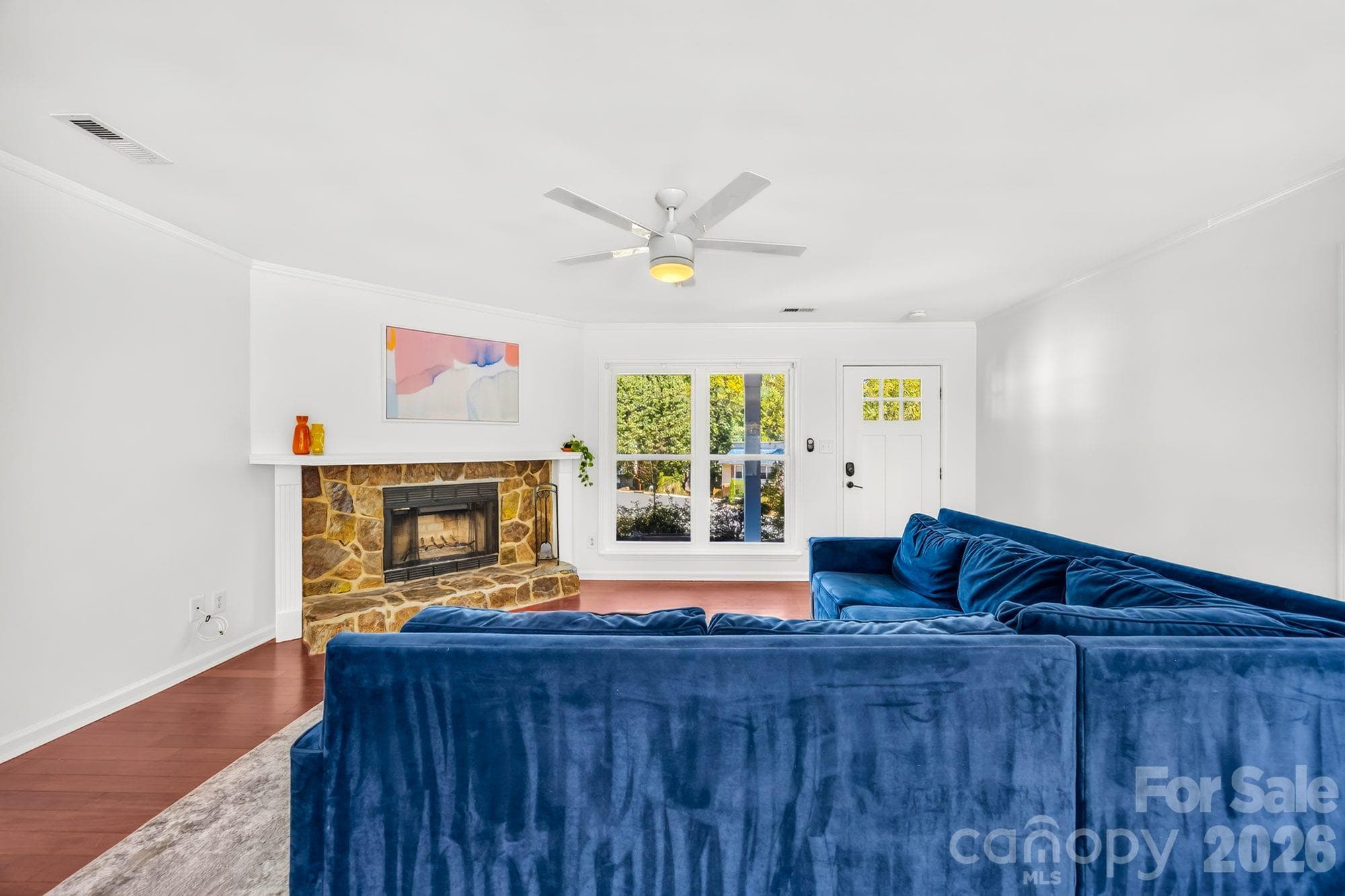 Living room with a stone wood-burning fireplace, wood floors and ceiling fan at 4900 Cricklewood Ln, Charlotte - 4900 Cricklewood Lane, Charlotte