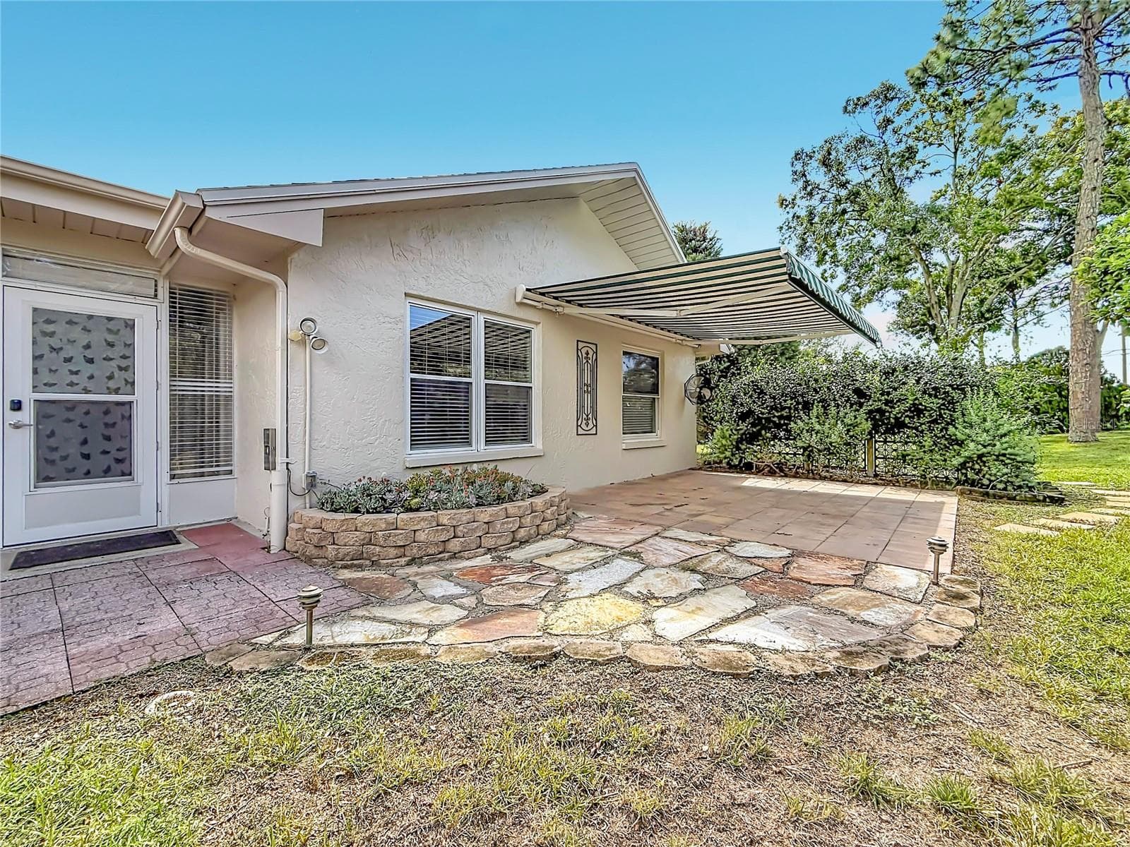 Patio with retractable awning overlooking Rear Green Space and Succulent Bed - 2632 CAMILLE DR, PALM HARBOR