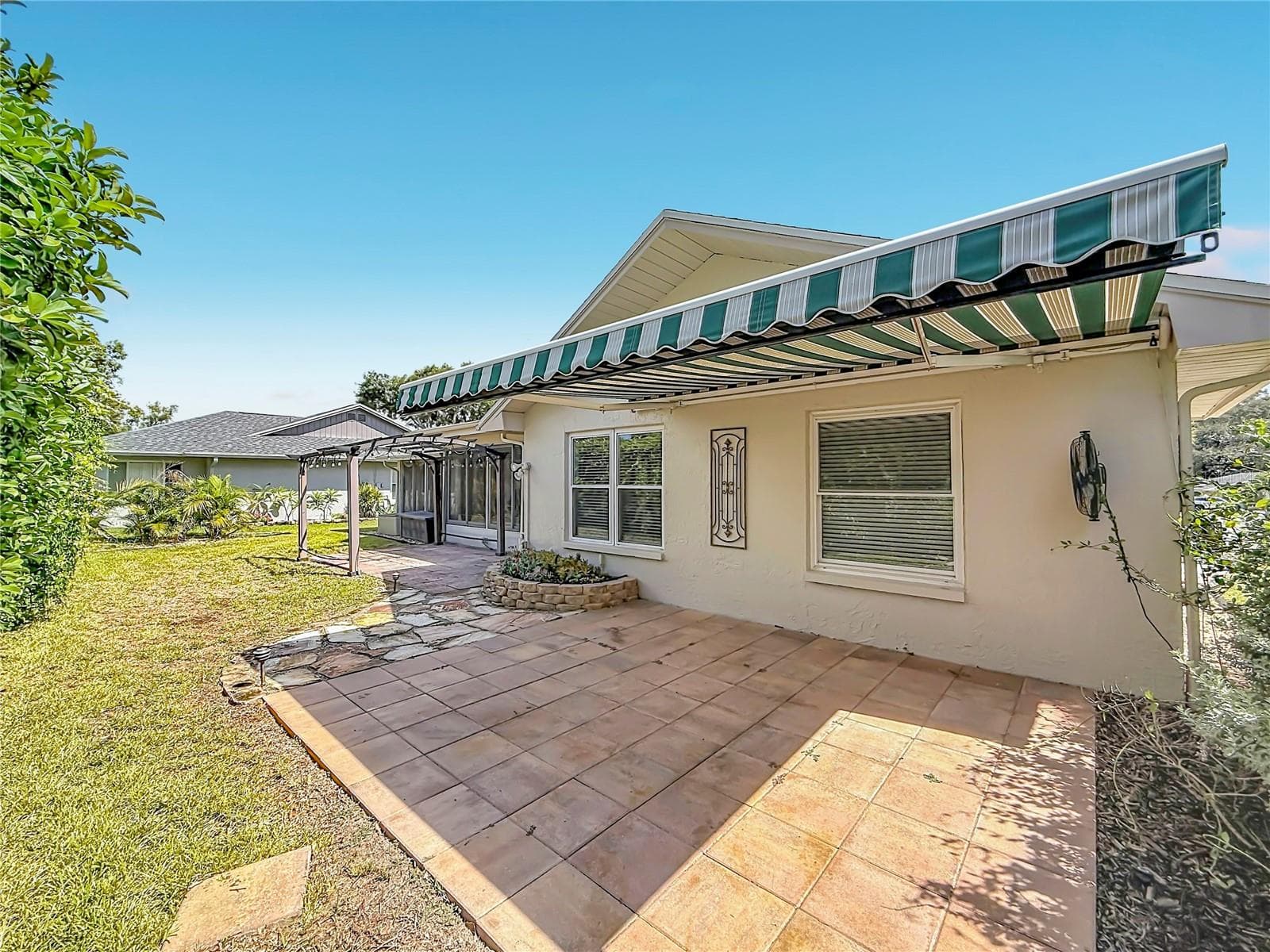 Patio with retractable awning overlooking Rear Green Space and Succulent Bed - 2632 CAMILLE DR, PALM HARBOR