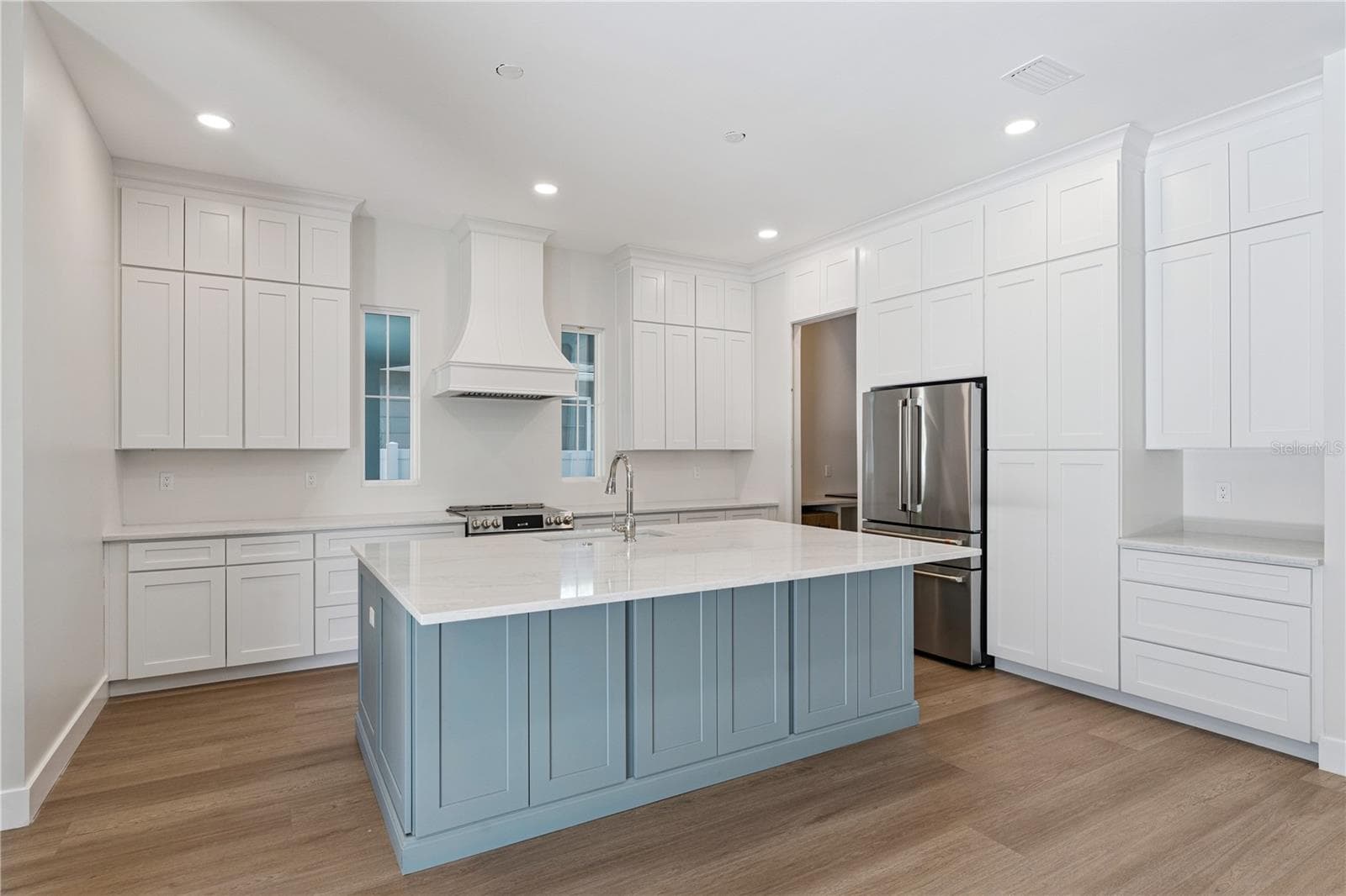 The main kitchen features a blue island, white cabinetry, a statement range hood, and stainless steel appliances. - 3456 FAIRWAY LN, ORLANDO