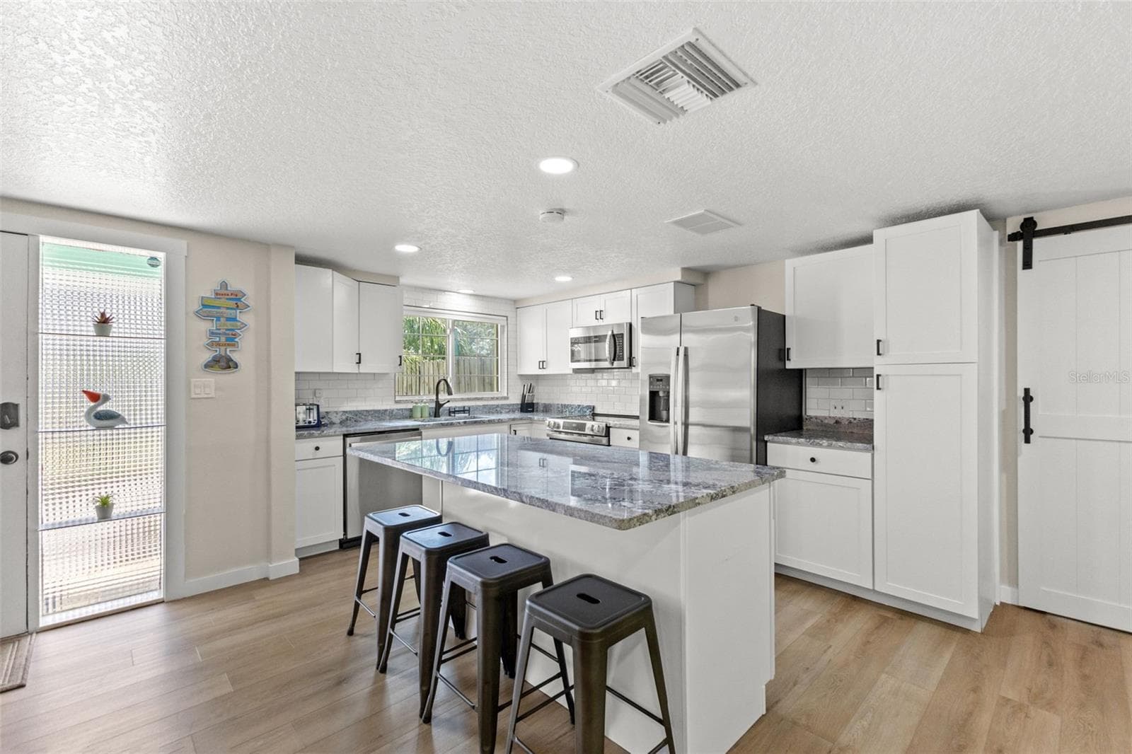 Bright, renovated kitchen with a large center island, seating for four, stainless steel appliances, and plenty of cabinet storage. - 201 SOUTH ST, PALM HARBOR