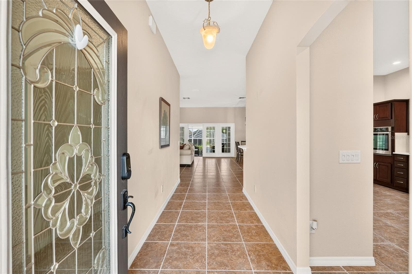 A decorative glass front door welcomes you into a bright foyer with tile flooring and an inviting view into the living spaces beyond. - 2454 MORNING DOVE LN, THE VILLAGES