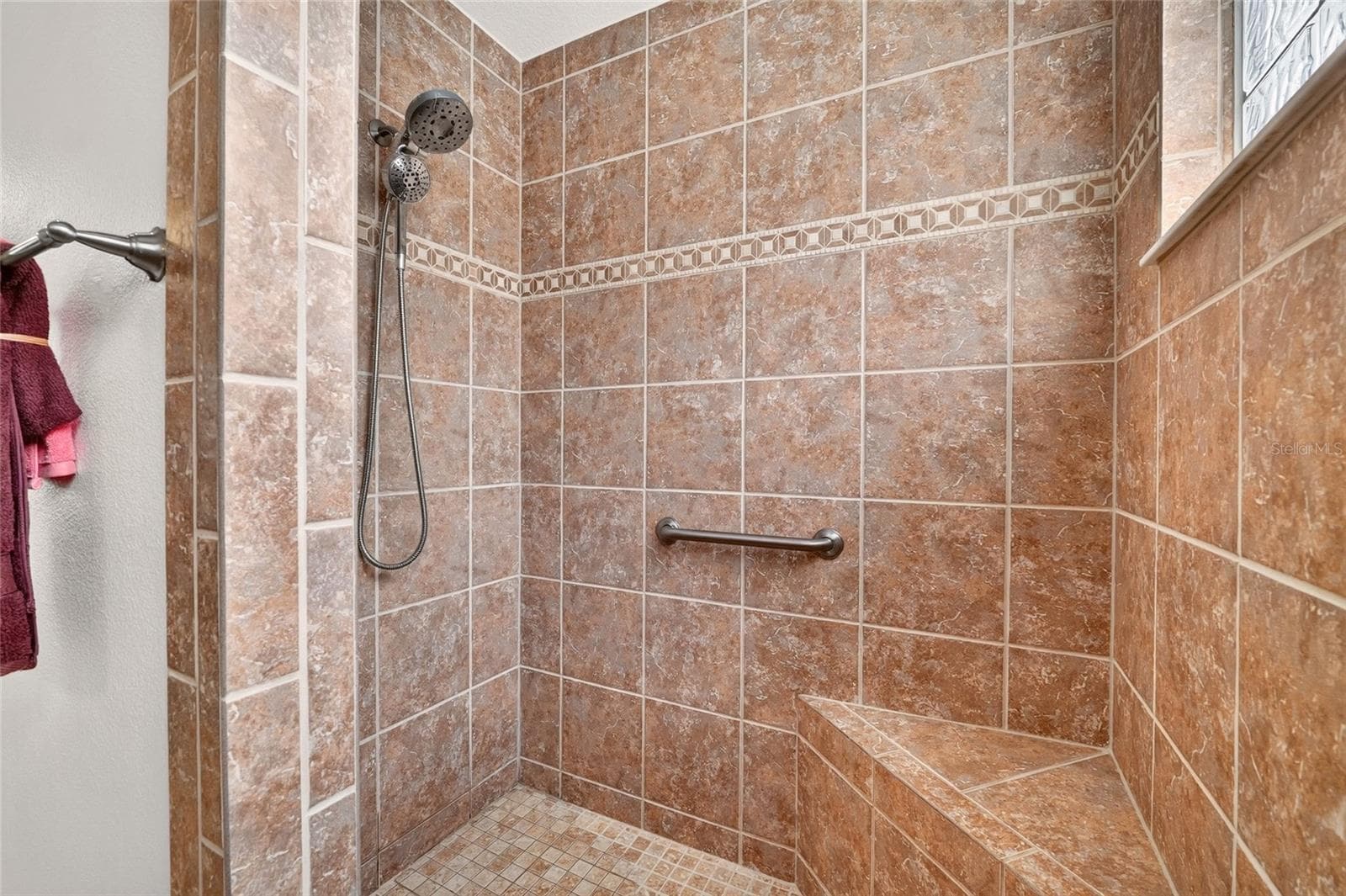 Enjoy a spacious ROMAN SHOWER with a convenient bench, decorative tile accents, and a GLASS-BLOCK WINDOW that welcomes natural light while maintaining privacy. - 2454 MORNING DOVE LN, THE VILLAGES
