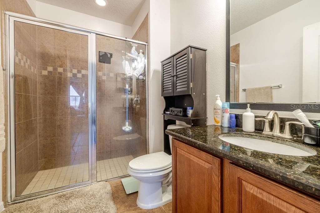 Ensuite bathroom to primary bedroom with tile shower and granite countertops - 252 SHERRI LEE LN, DELAND