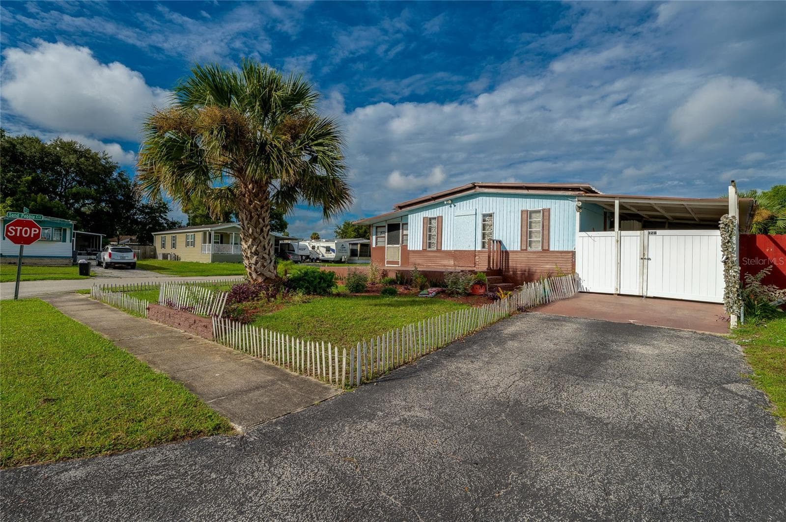 Front view showcases the home’s landscaped yard, mature palm tree, driveway, covered parking area, and welcoming entry. - 128 KON TIKI TER, PORT ORANGE