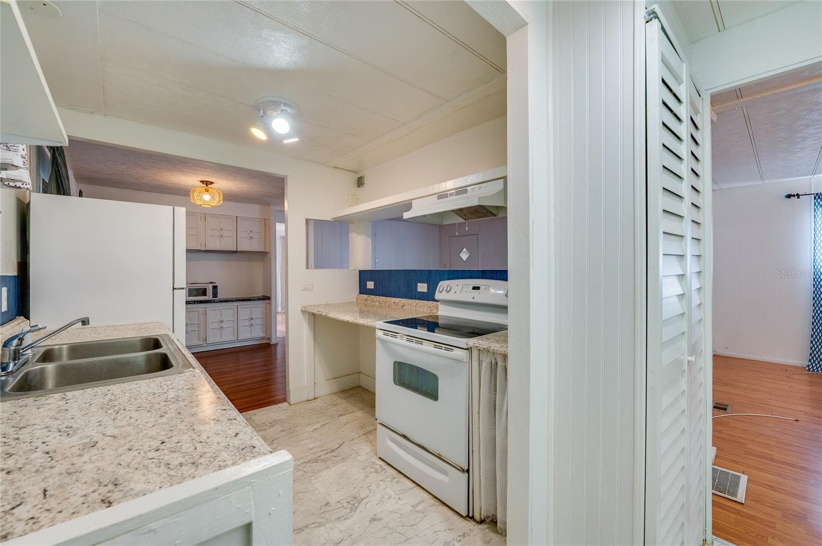 Functional eat-in kitchen features generous counter space, a double-basin sink, range with hood, refrigerator, and a pass-through opening that connects with the adjoining living area. - 128 KON TIKI TER, PORT ORANGE