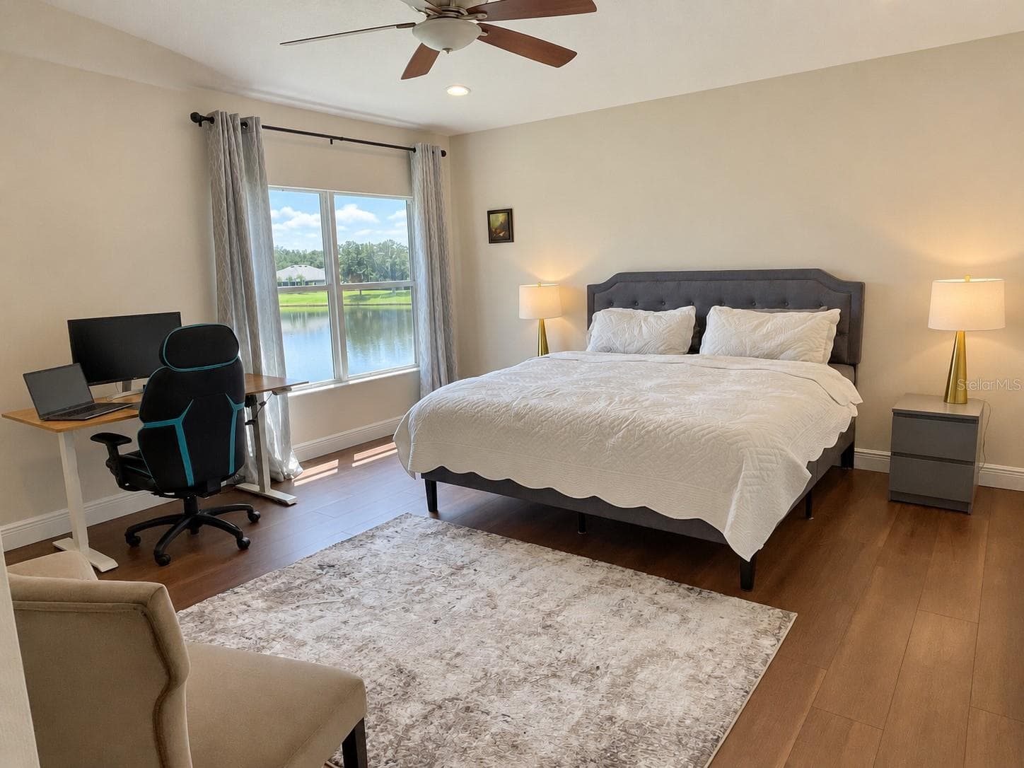 A spacious bedroom with water views, a large window, and room for both a sitting area and a desk. An upholstered bed, soft neutral finishes, and a ceiling fan complete the space. - 11117 ANCIENT FUTURES DR, TAMPA
