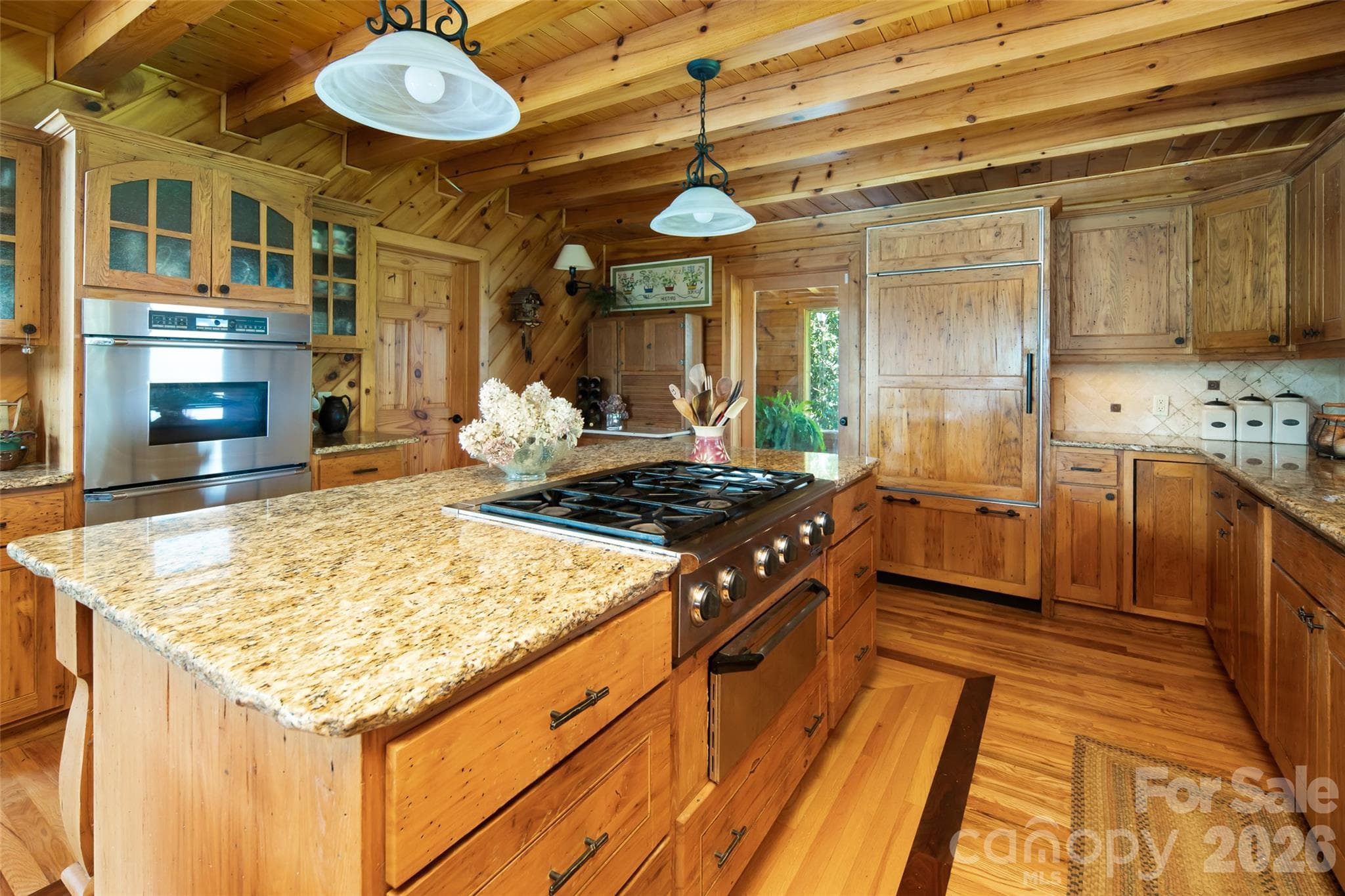 Kitchen island with gas range. Double oven behind. Refrigerator at back center blends in with the cabinetry for a sleek, seamless look. Granite countertops. - 316 Stevenson Cove Road, Waynesville
