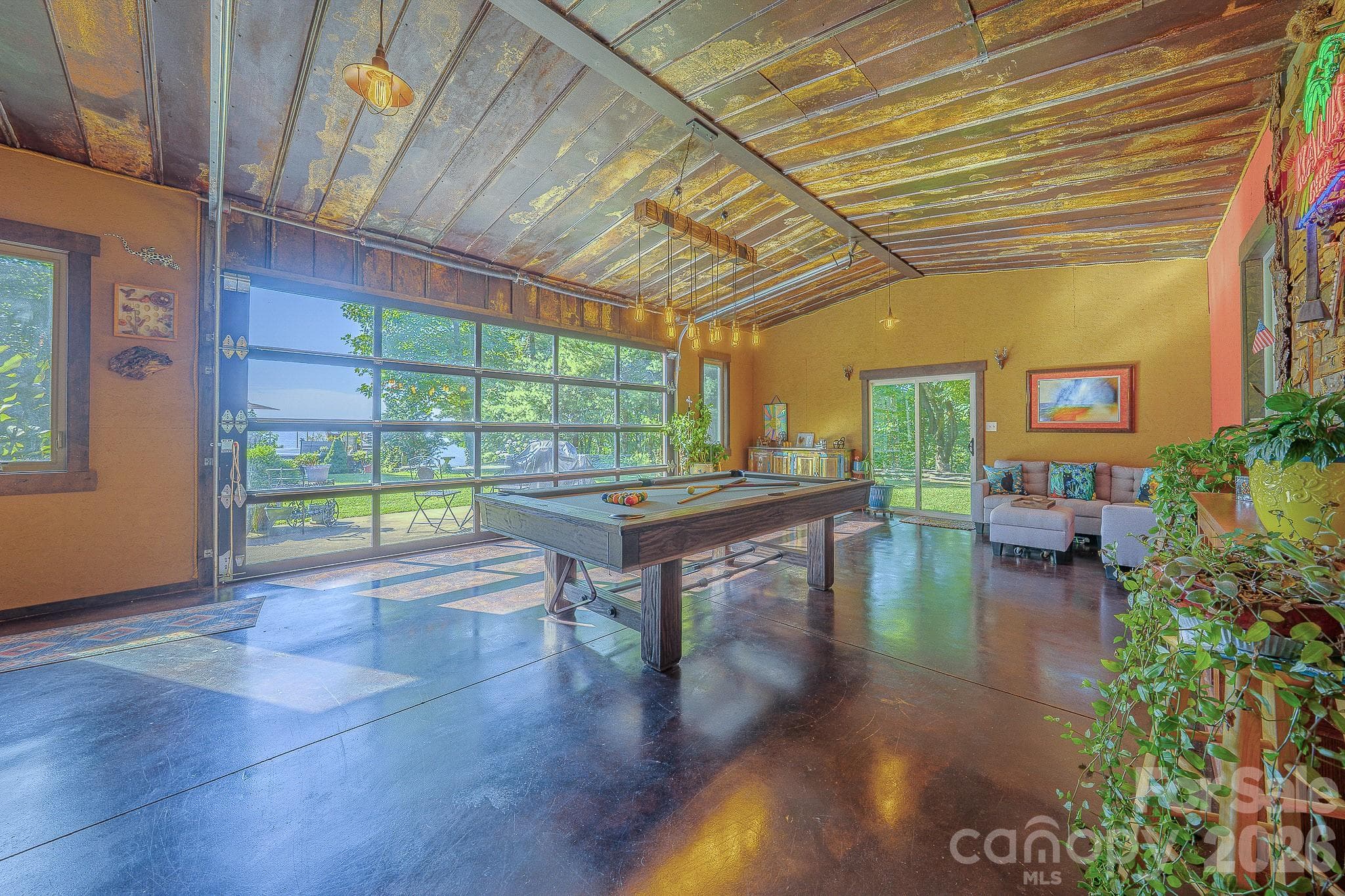 Stained concrete floors, rustic metal ceilings, and an insulated glass garage door make the recreation room a standout in this Old Fort, NC home, near Black Mountain & Asheville. - 54 Winning Way, Old Fort