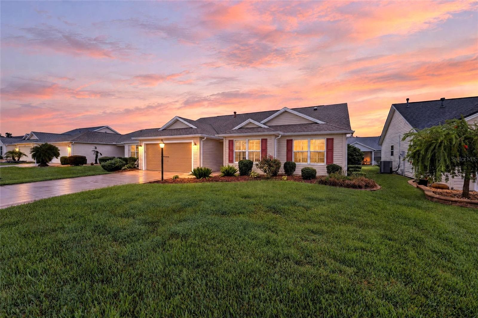 Beautiful twilight view showcasing the home's inviting exterior, illuminated windows, manicured landscaping, and spacious front lawn beneath a colorful sunset sky. - 3064 BURBANK LN, THE VILLAGES