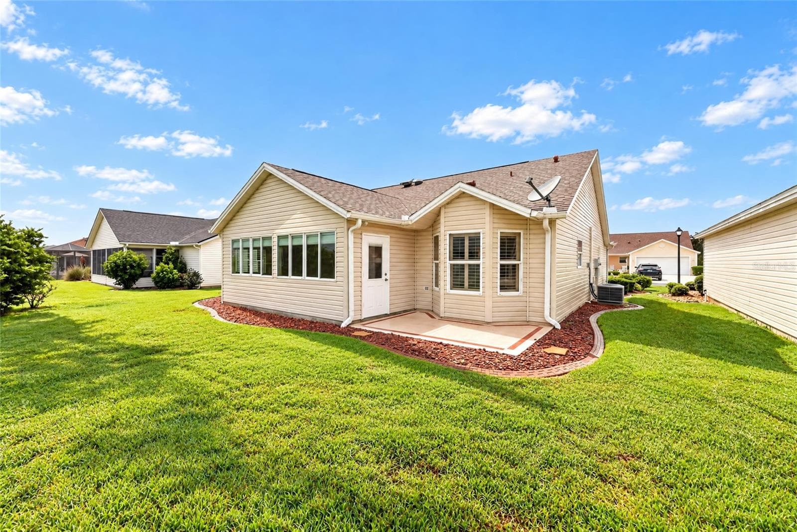 Rear exterior showcasing a spacious lawn, mature landscaping, attractive rooflines, and a convenient rear entry with a decorative patio area. - 3064 BURBANK LN, THE VILLAGES