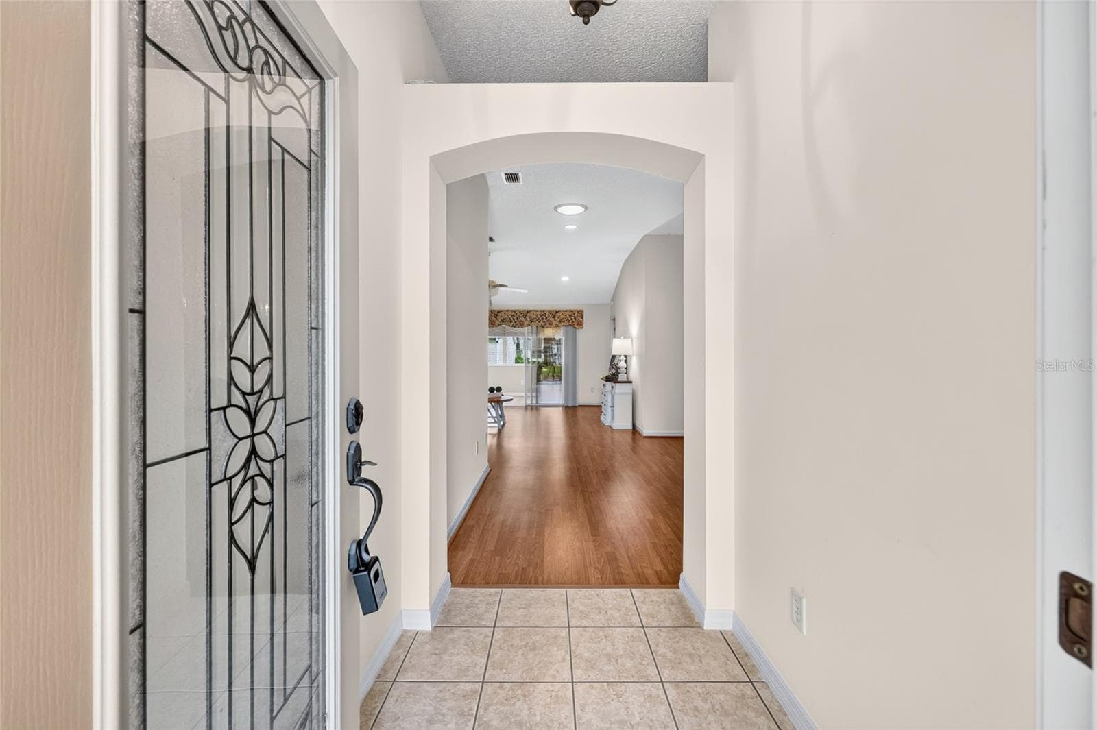 Inviting foyer featuring a decorative glass front door, tile flooring, and an elegant arched opening leading into the main living area. - 3064 BURBANK LN, THE VILLAGES